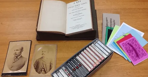 Collection of historical items including photographs, an open book, and cassette tapes, representing primary source materials preserved at the Amistad Research Center.