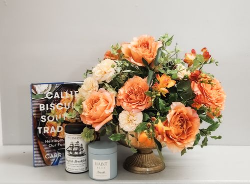 Amber Honey floral arrangement featuring warm-toned roses, golden seasonal blooms, textured greenery, and autumn accents in an organic, low centerpiece design