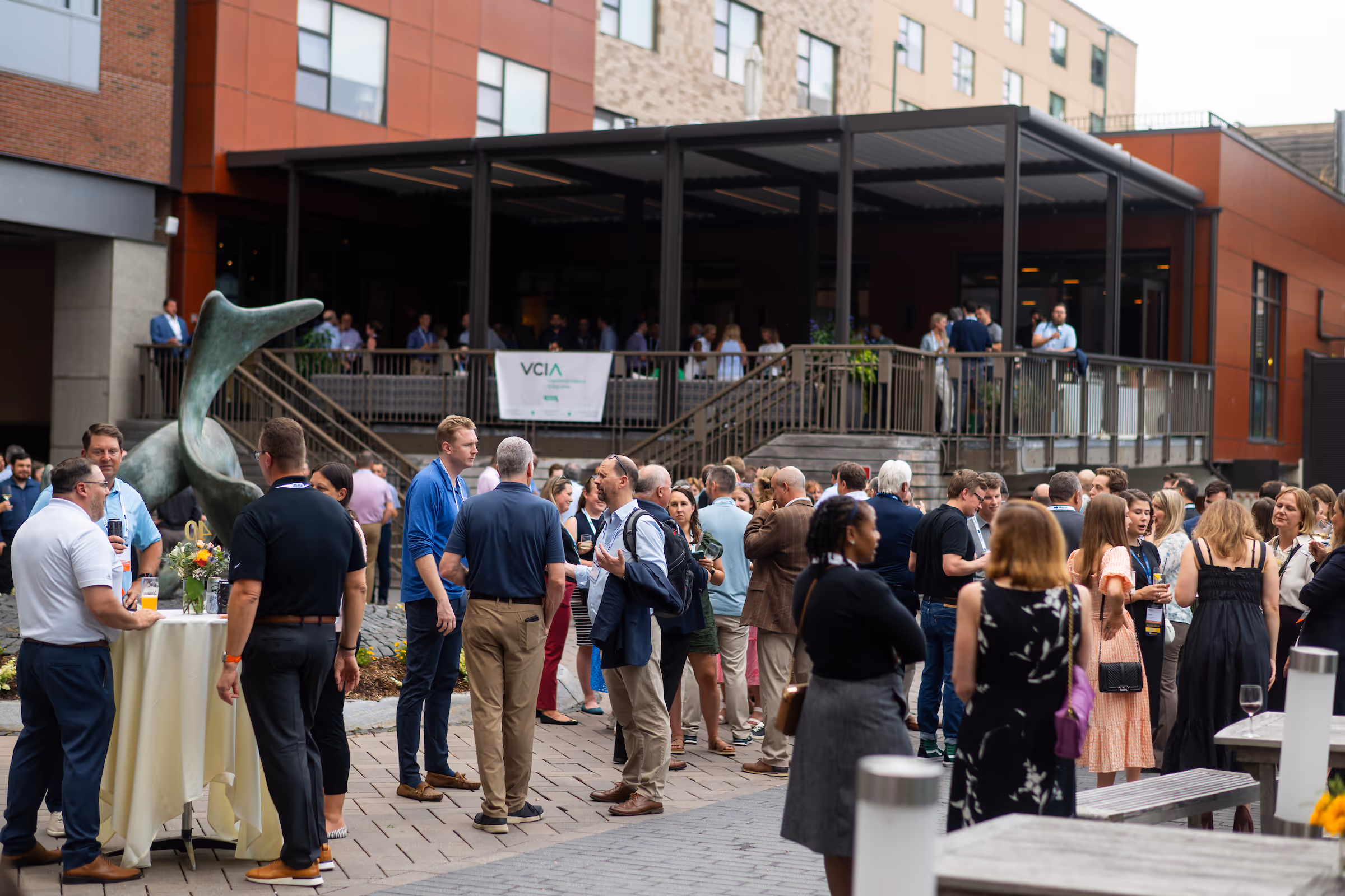 Outdoor captive insurance networking event with groups of captive insurance professionals conversing near a modern building and a large abstract sculpture.