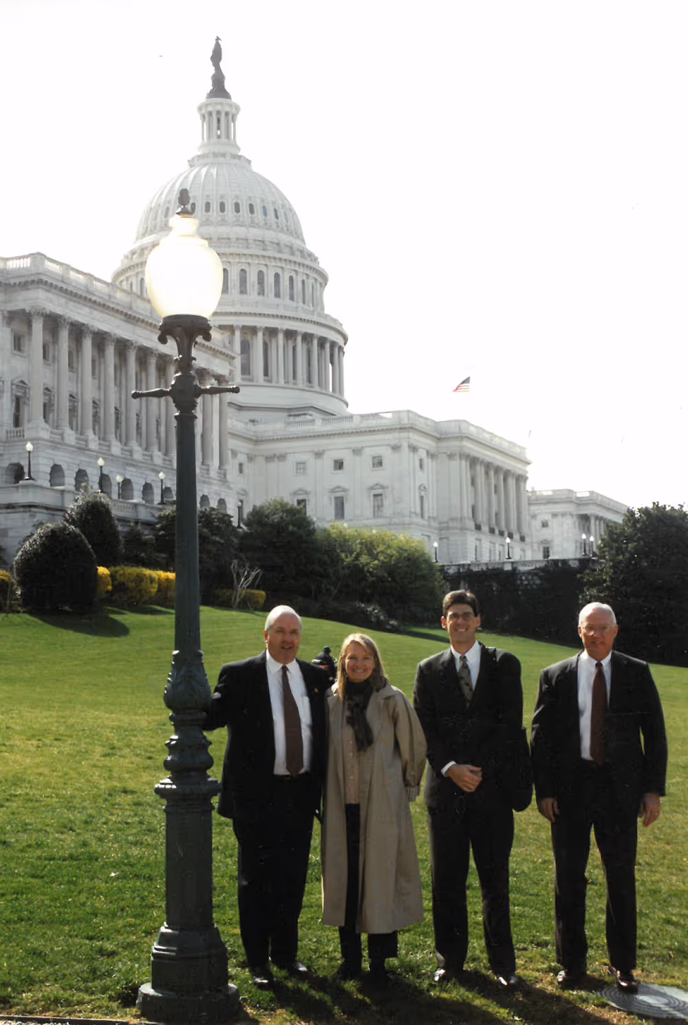 Four people standing on grass in front of the US Capitol building on a sunny day.