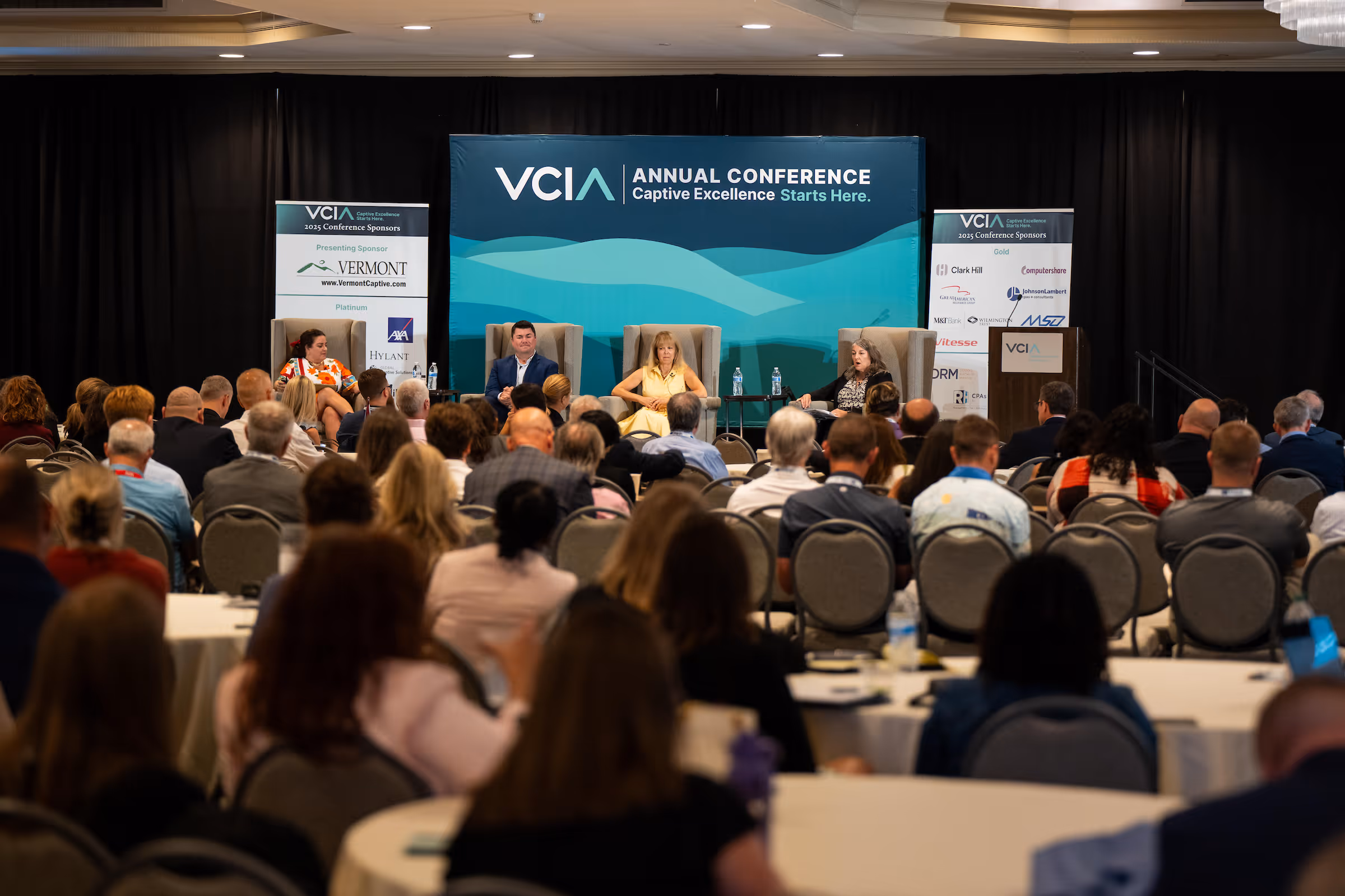 Panel of four speakers seated on stage at the VCIA Annual Conference with an audience facing them in a large conference room.
