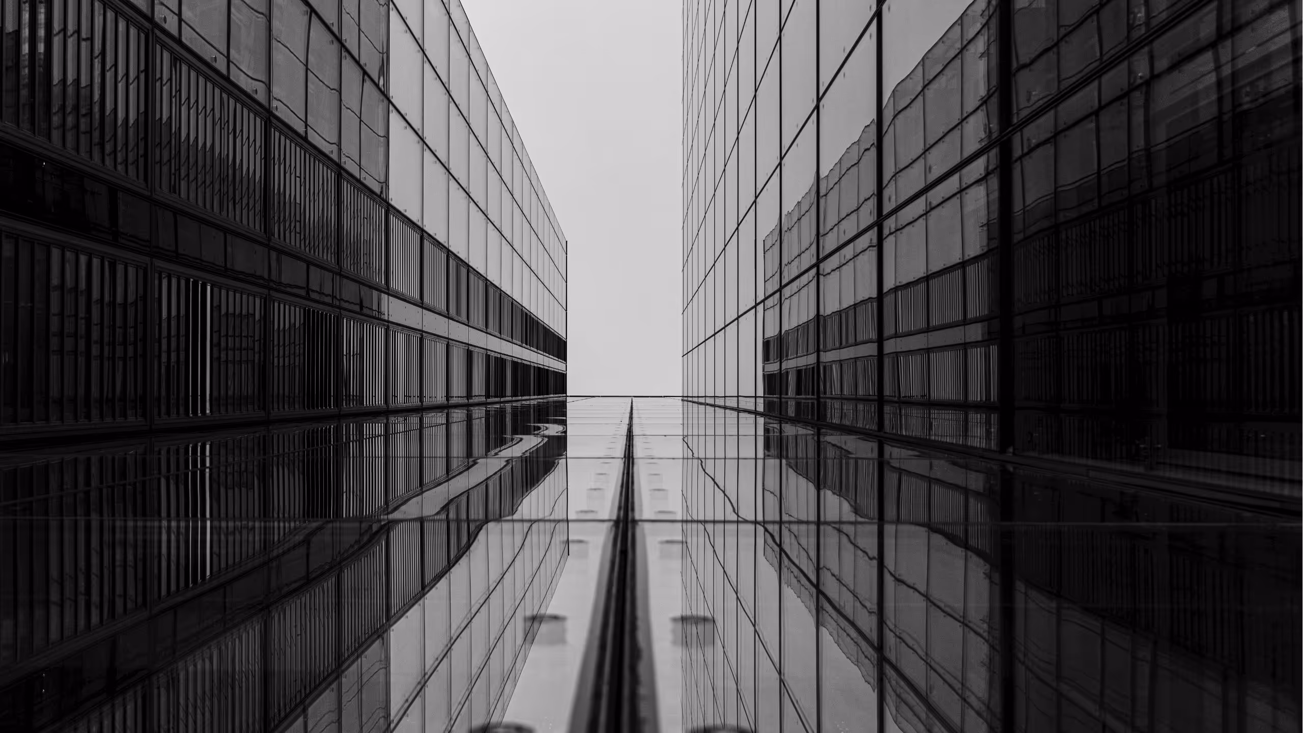 Black and white photo looking upwards between two modern glass skyscrapers reflecting each other.