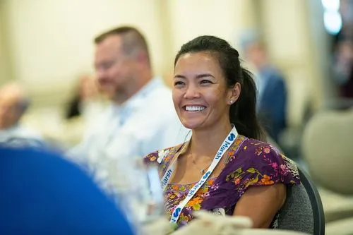 Smiling woman wearing a purple floral dress and a Marsh lanyard at a conference.