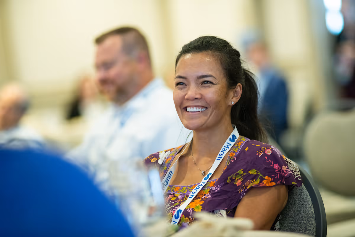 Smiling woman wearing a purple floral dress and a Marsh lanyard at a conference.