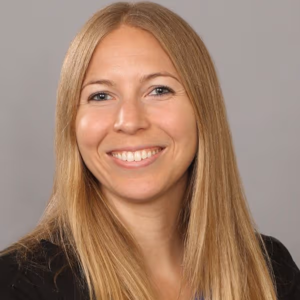 Woman with long blonde hair smiling against a gray background.