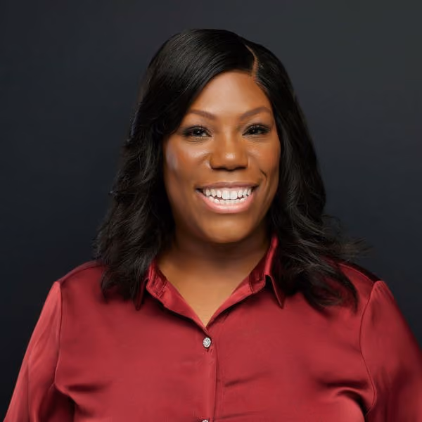 Smiling woman with shoulder-length black hair wearing a red blouse against a dark background.