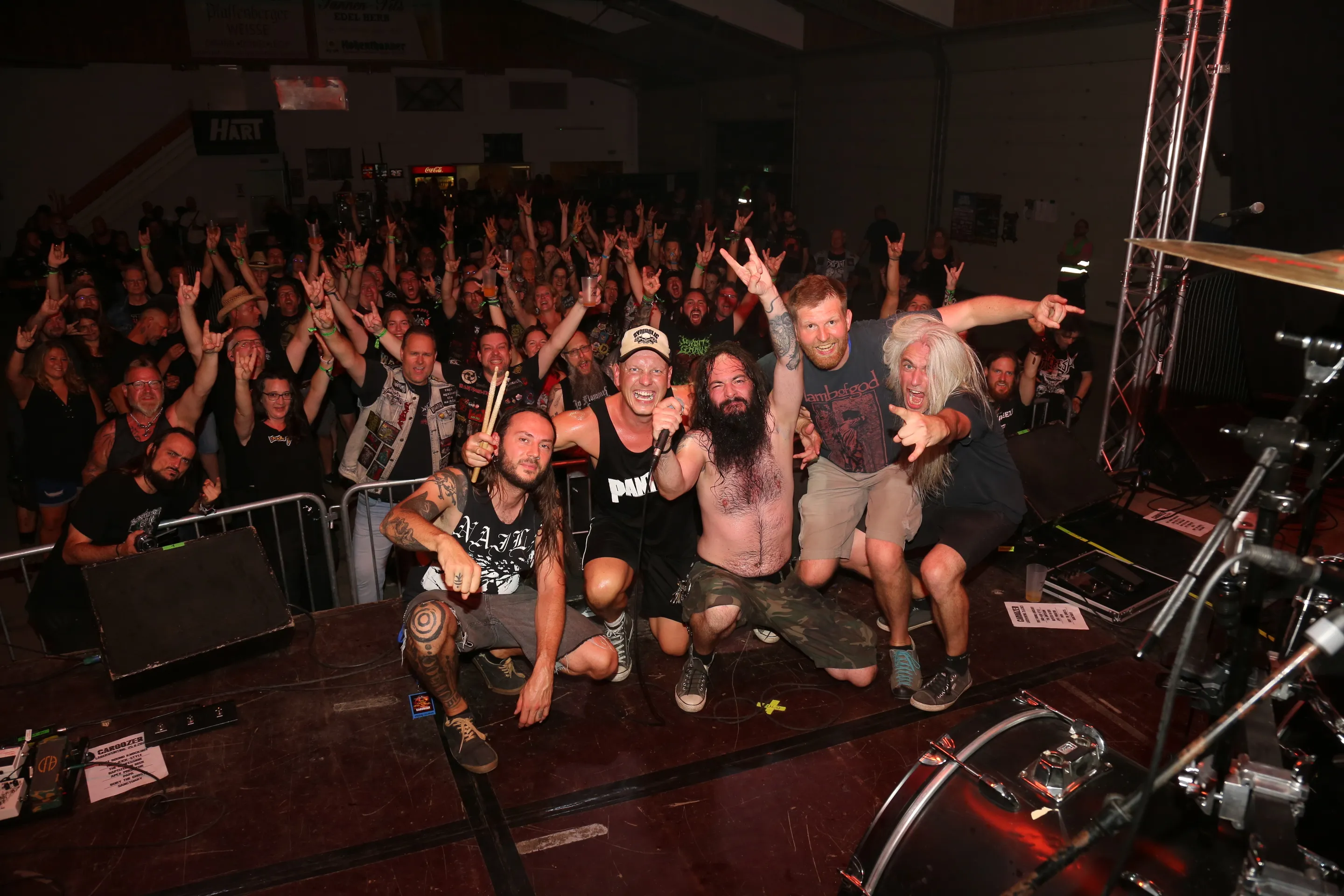 Five band members posing on stage in front of an enthusiastic crowd during a live rock concert.