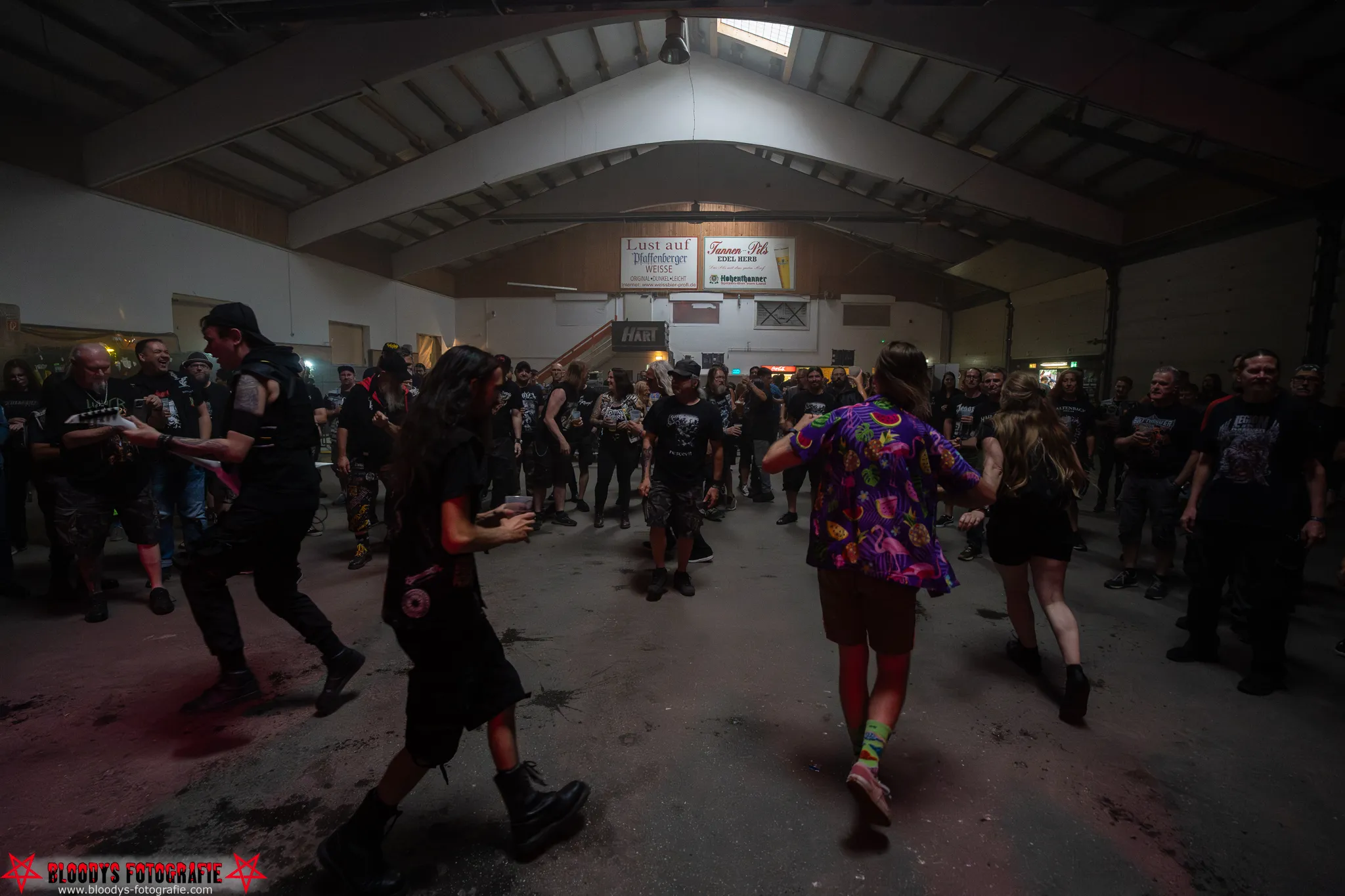 Crowd of people at an indoor concert or event in a large warehouse-like space with dim lighting.