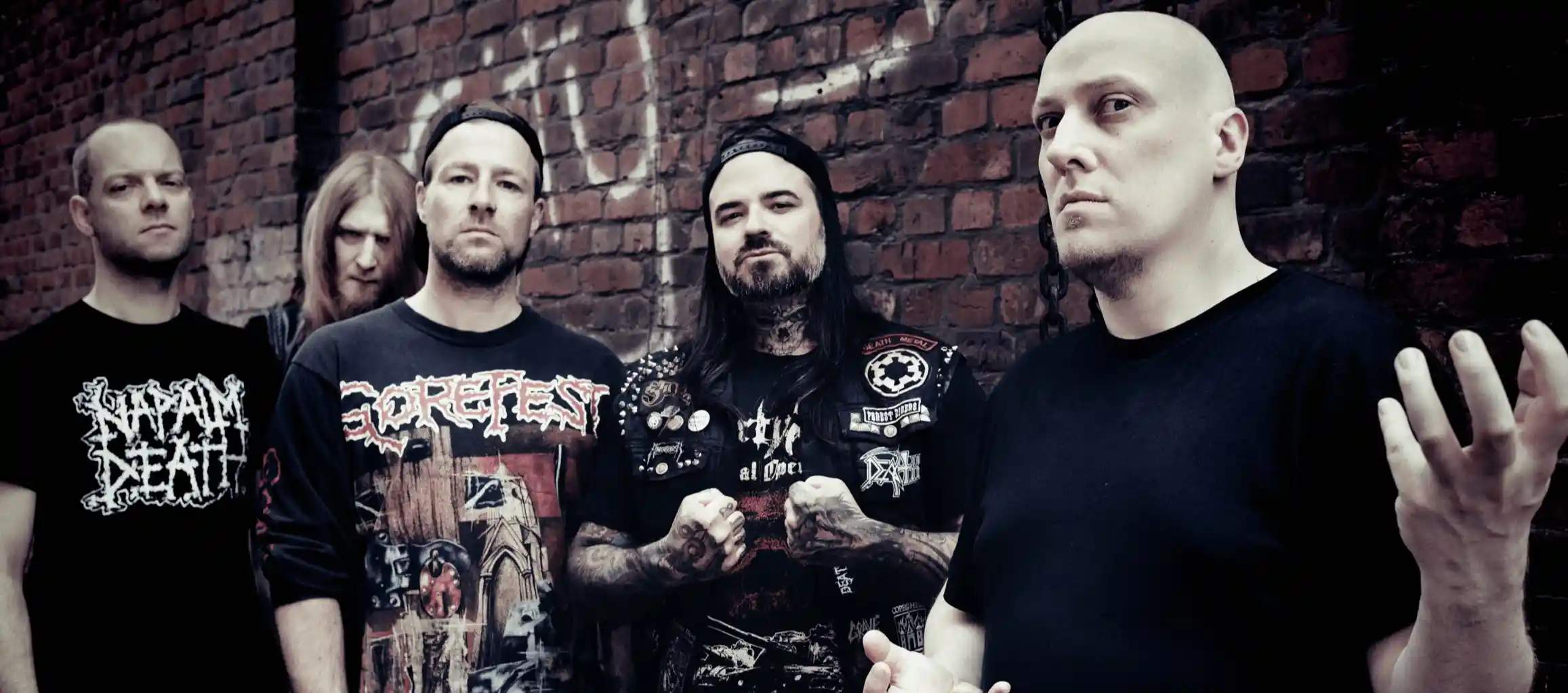 Five men with serious expressions standing against a graffiti-covered brick wall, wearing band and metal-themed clothing. Band: ENDSEEKER