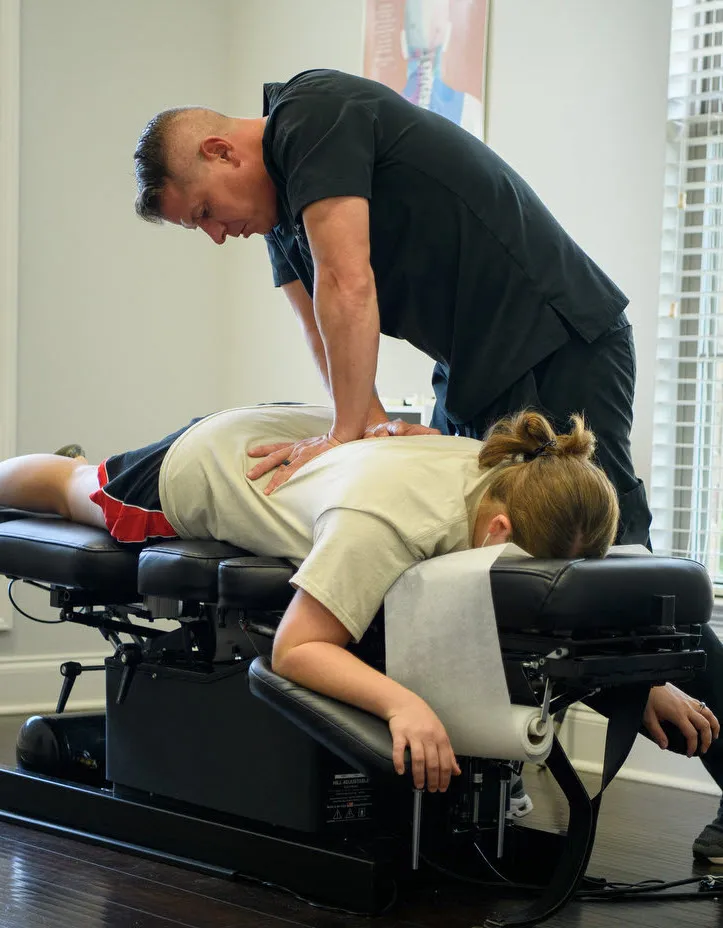 A chiropractic delivering a chiropractic treatment to a patient on a chiropractic table.