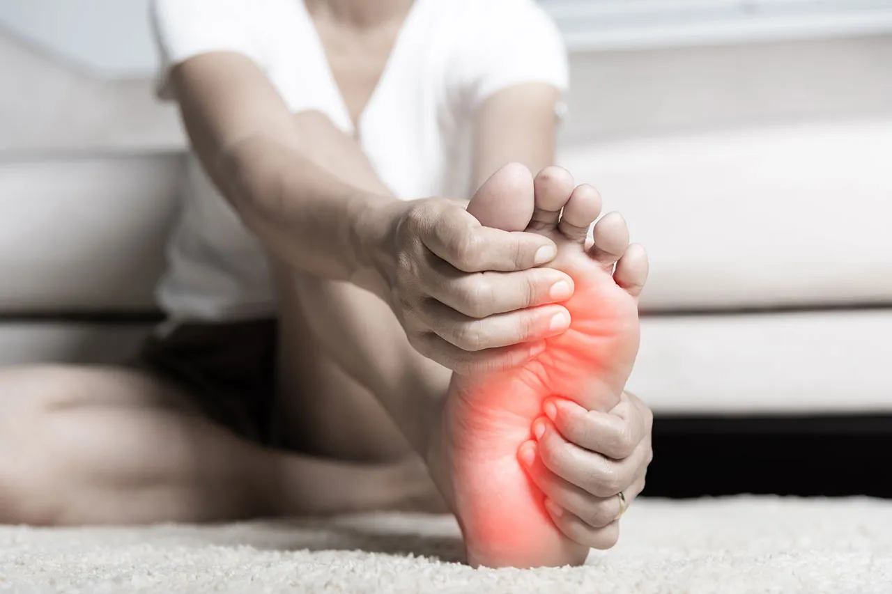 Neuropathy treatment concept: A patient is holding a painful foot, shown by added red color on the bottom of their foot, suggesting peripheral neuropathy.