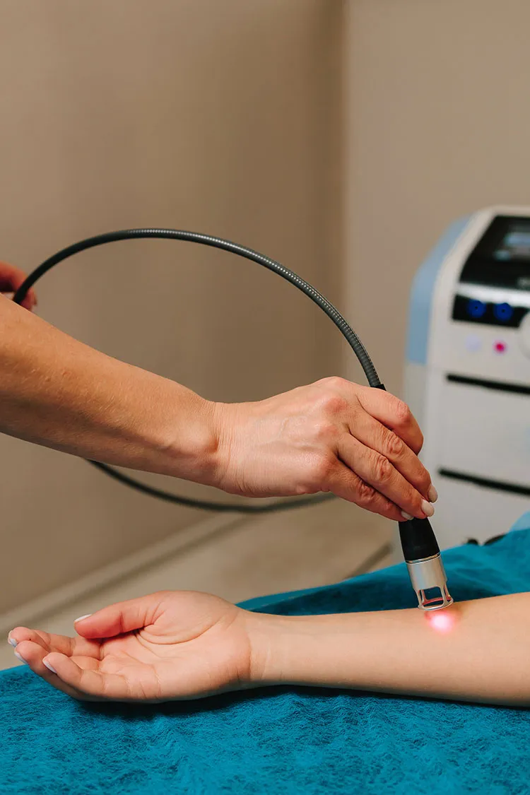 A therapist is holding a cold laser over a patient's tendons in the forearm.