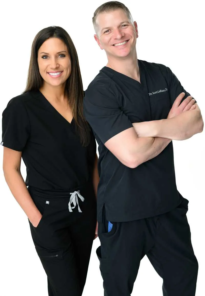 Dr. Scott LeBlanc, D.C., and Dr. Dana LeBlanc, D.C., chiropractors in Baton Rouge, standing in front of their chiropractic office, smiling, under the LeBlanc Spine Center sign.