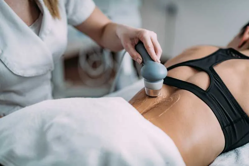 Physiotherapy modalities concept: A clinician is performing therapeutic ultrasound on the lower back of a female patient who is lying prone on a table.