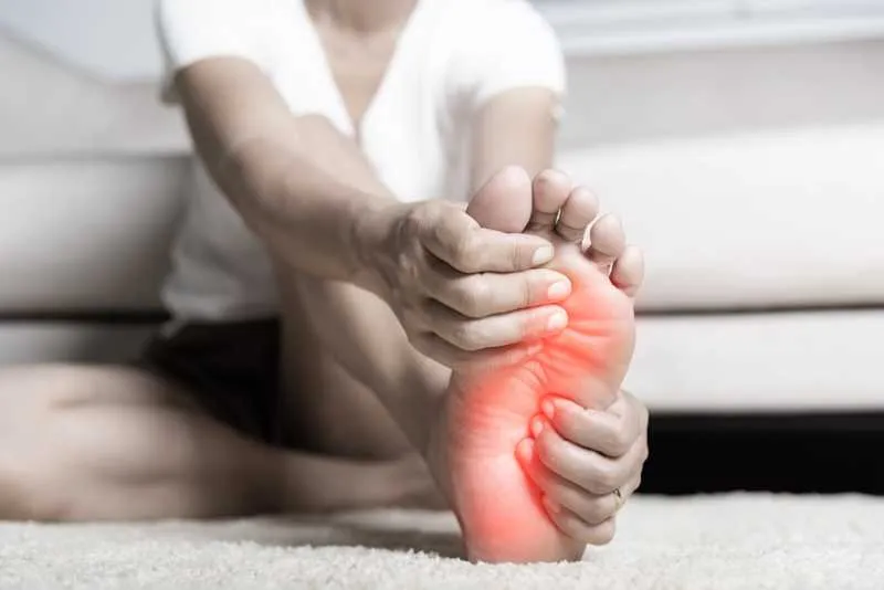 Neuropathy treatment concept: A patient is holding a painful foot, shown by added red color on the bottom of their foot, suggesting peripheral neuropathy.