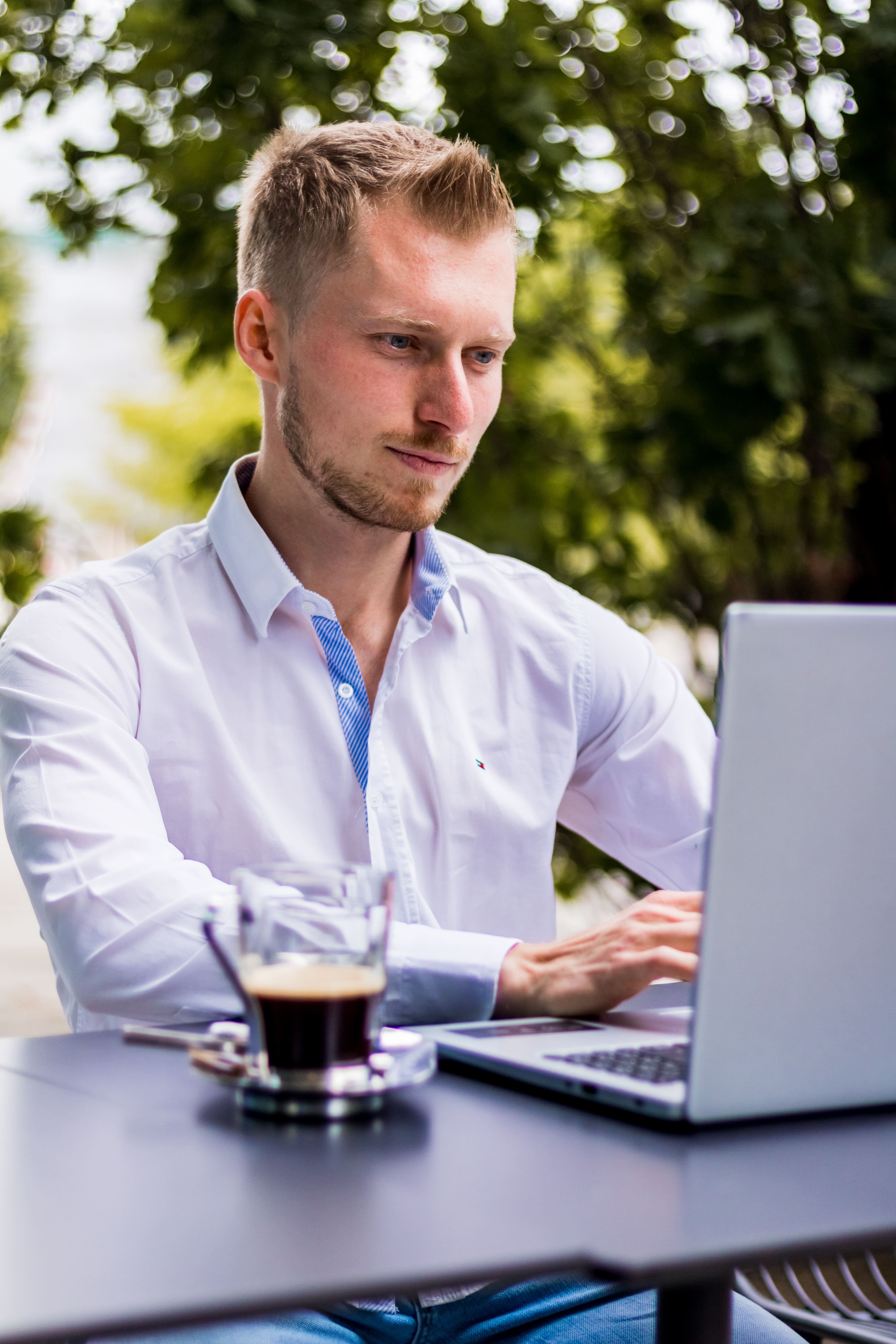 James Blond ist sitzend abgebildet und forkusiert vor einem aufgeklappten Laptop und einem K
affee daneben