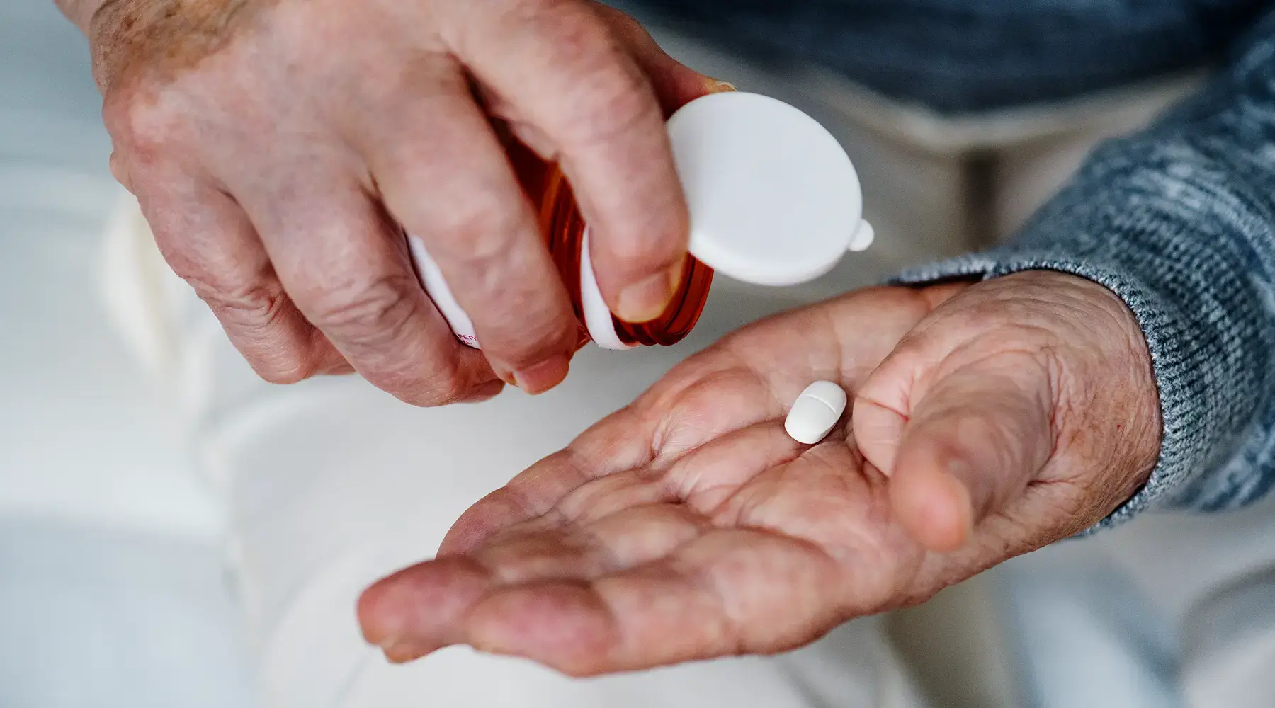 Older adult's hands pouring a single white tablet from a prescription bottle, illustrating medication use in a clinical trial
