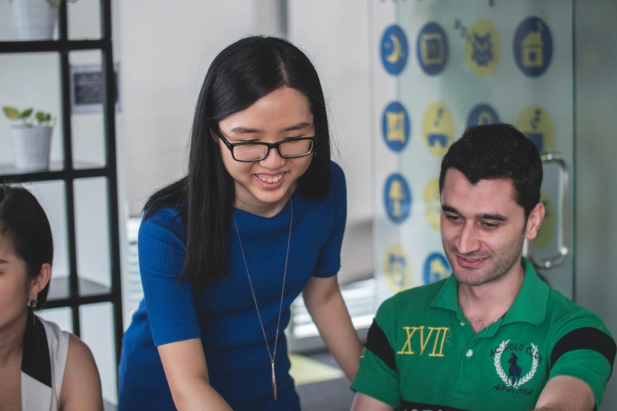 smiling woman standing beside smiling man pointing MacBook