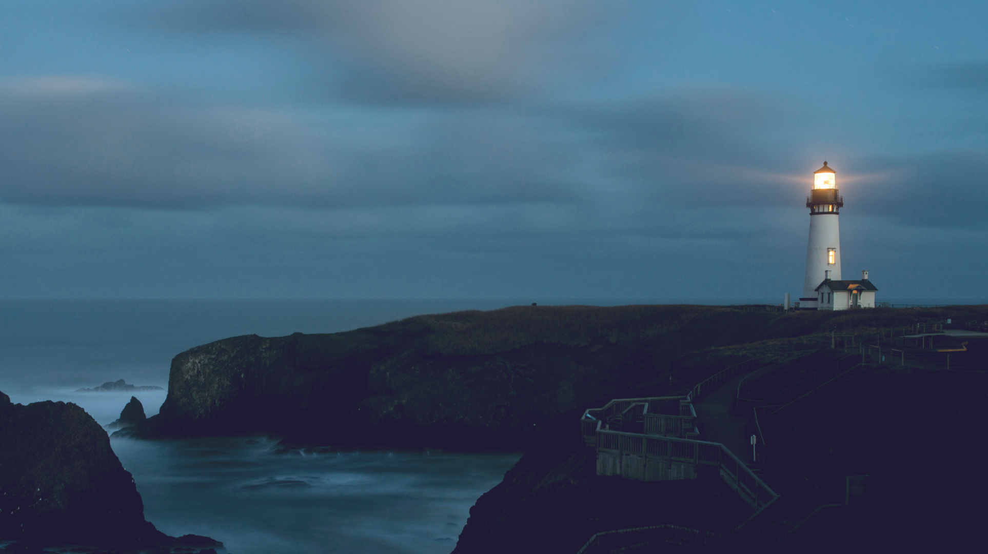 Lighthouse overlooking a rugged coastline at dusk, with its beacon shining across the sea to symbolise guidance, stability and confidence.