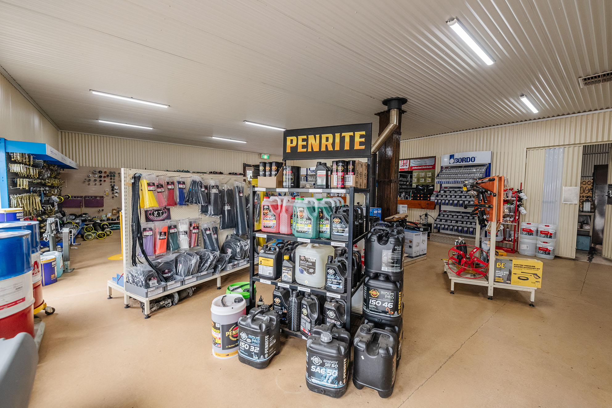 Interior of a hardware or automotive store featuring shelves stocked with oils, tools, and accessories, including a prominent Penrite display stand.