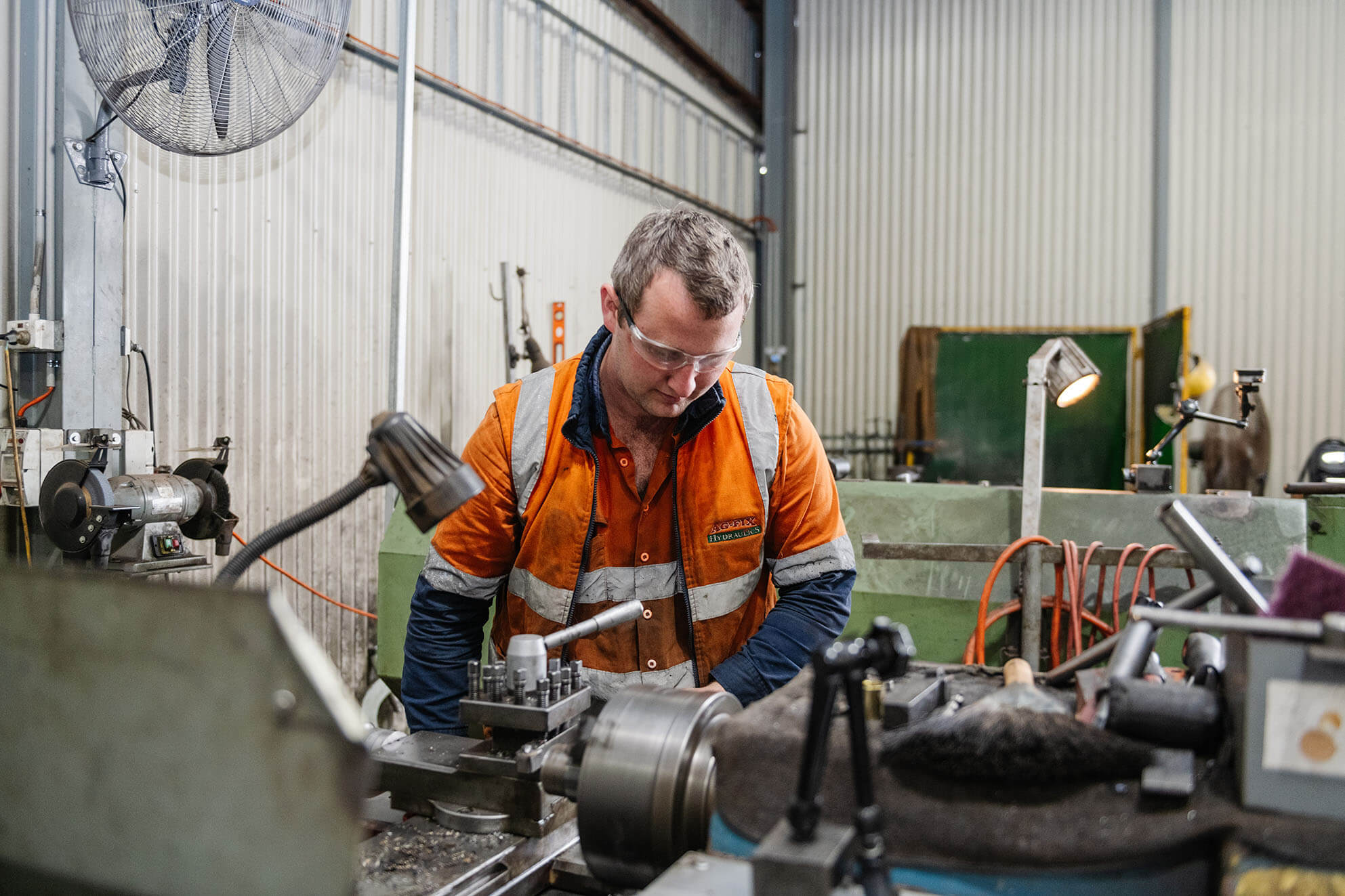 Worker in orange vest operating machinery during hydraulic repair.