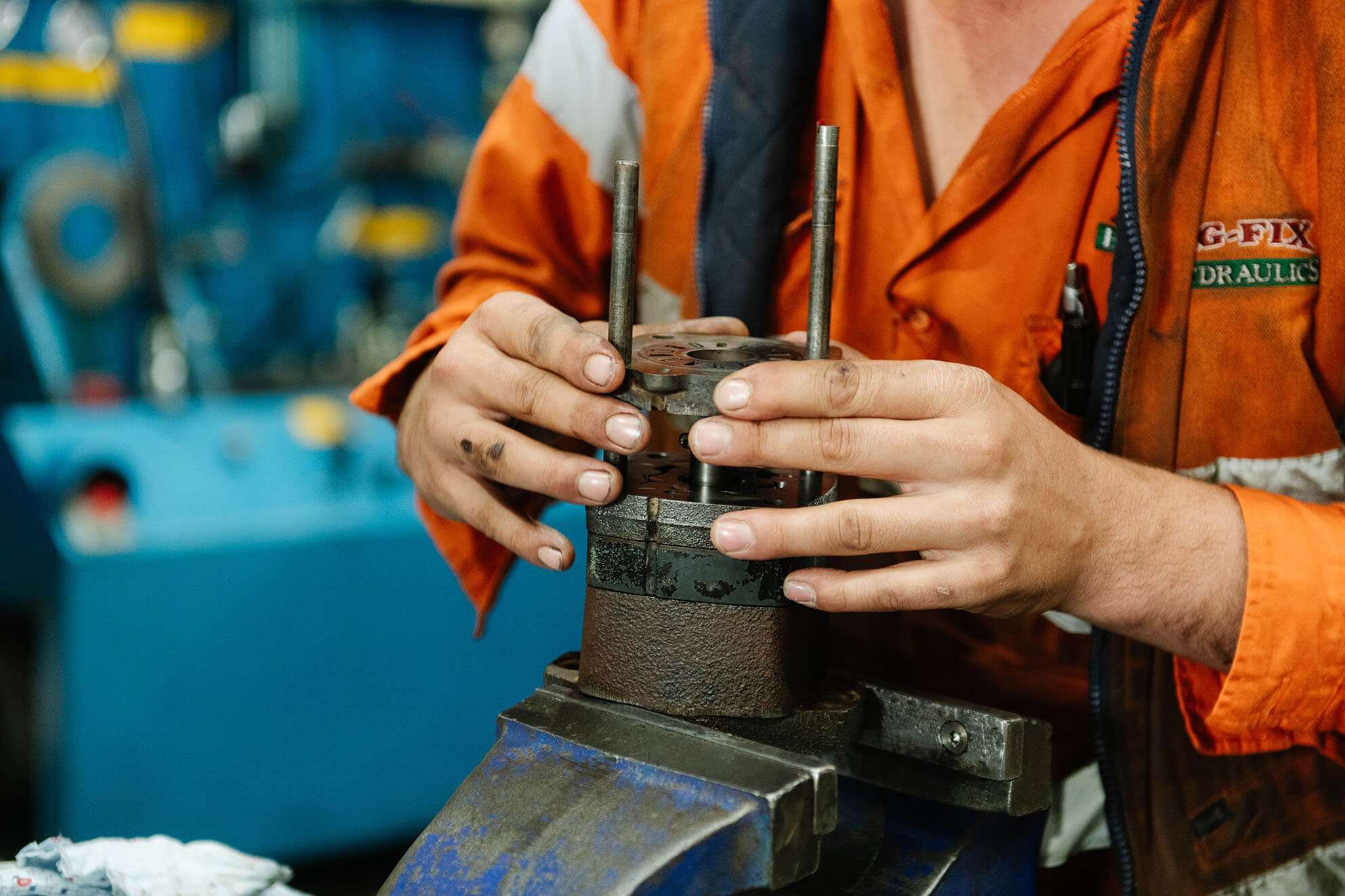 Worker in orange uniform repairing hydraulic component in workshop.