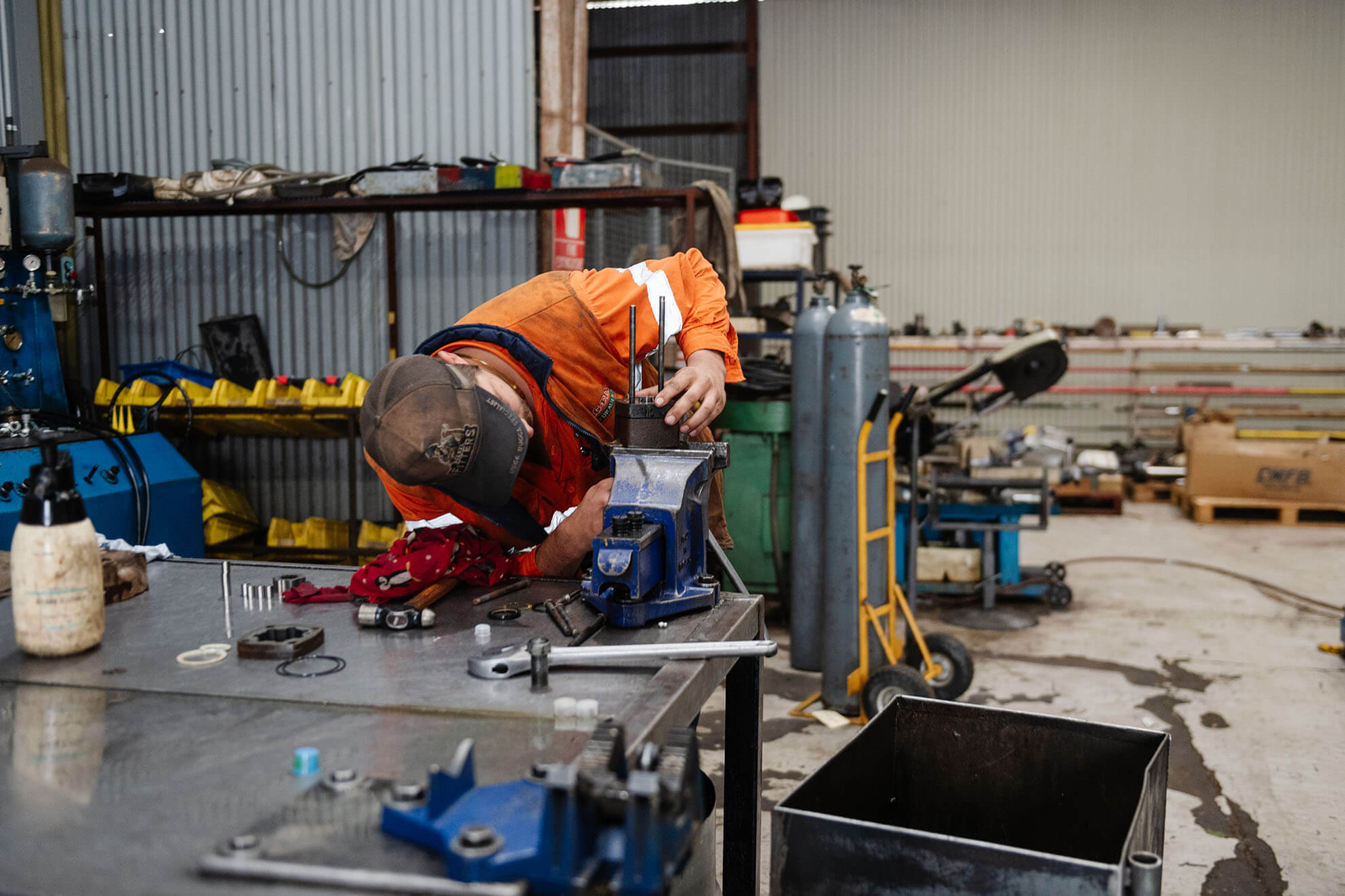 Worker in safety gear using tools to repair machinery in workshop.