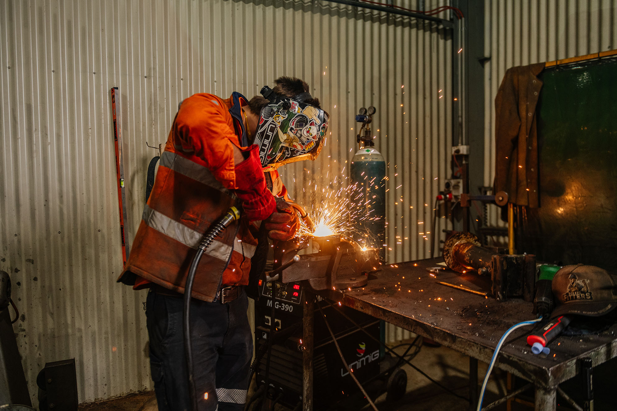 Worker in high-visibility clothing and protective gear welding metal in an industrial workshop, with sparks flying around the work area.