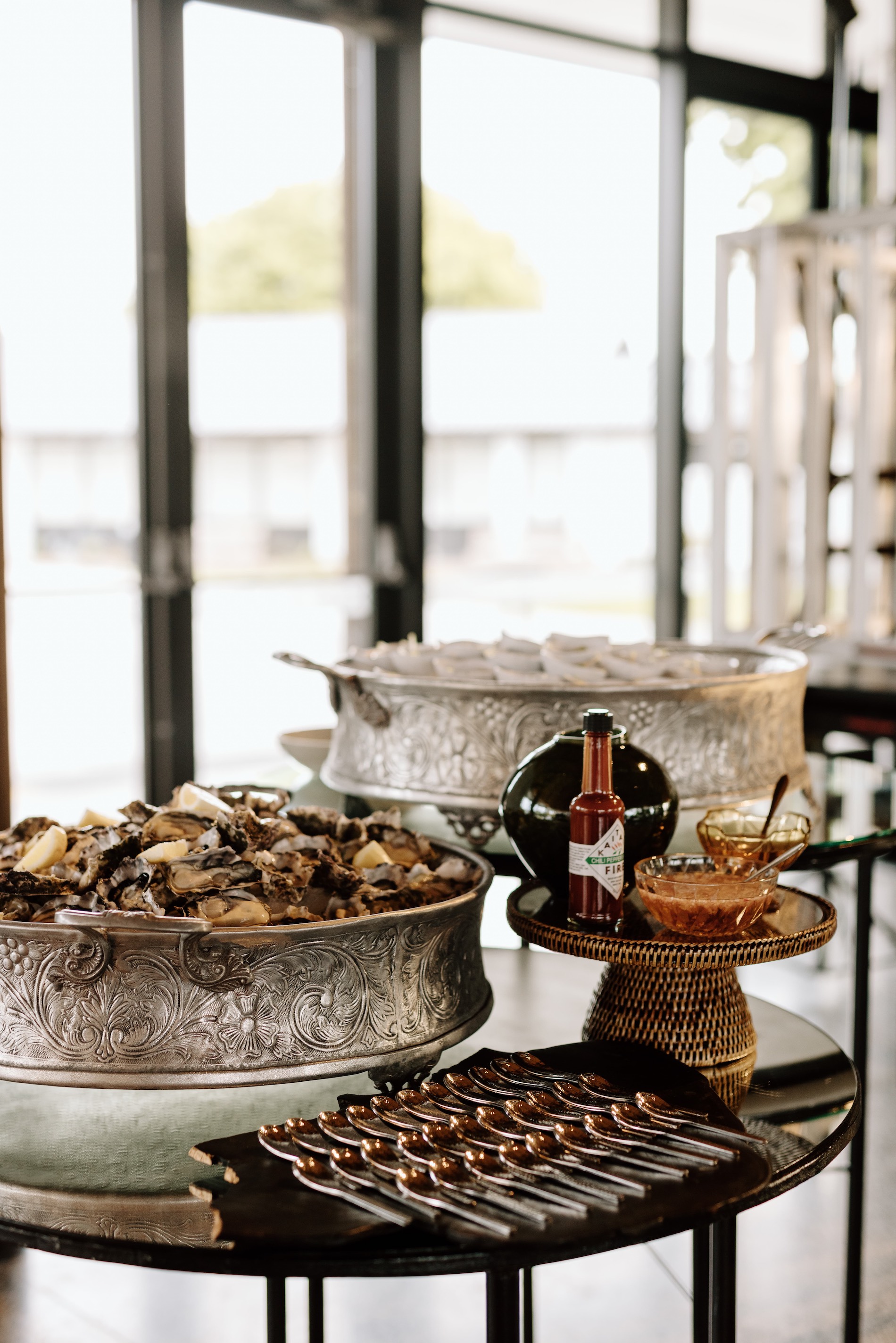 Tiered serving platters displaying appetizers and desserts on a table near windows.