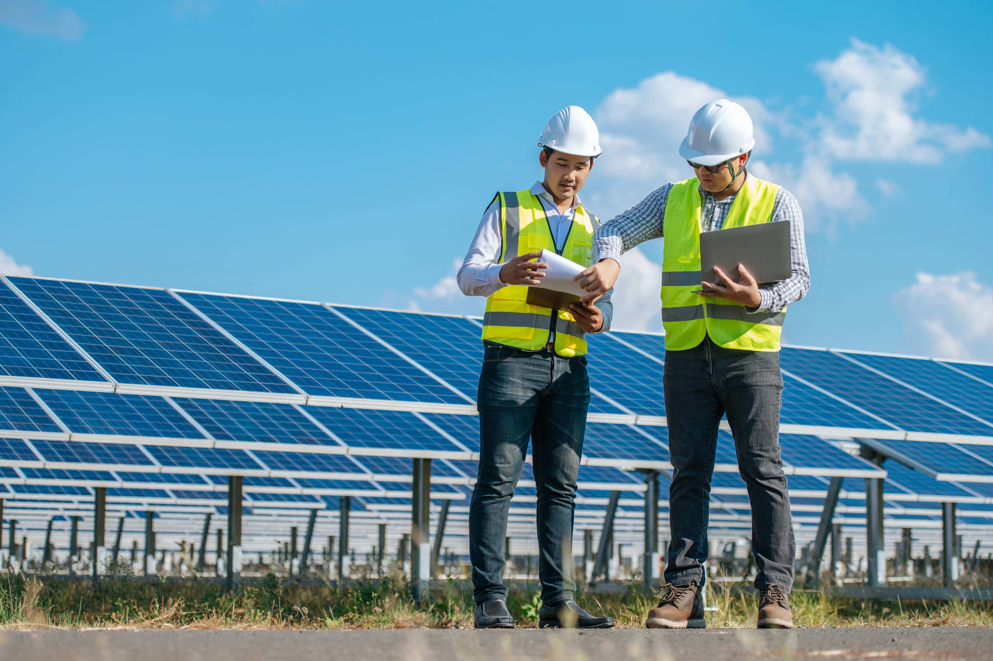 Two asian young engineers walking along rows of photovoltaic panels
