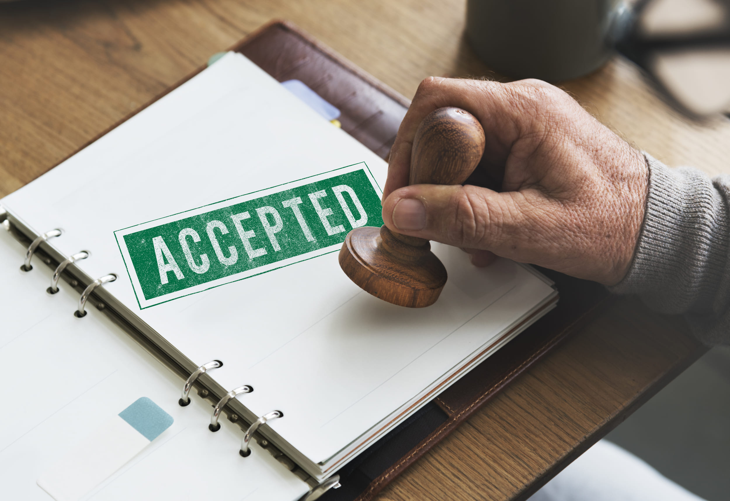 Hand stamps 'ACCEPTED' in green on notebook
