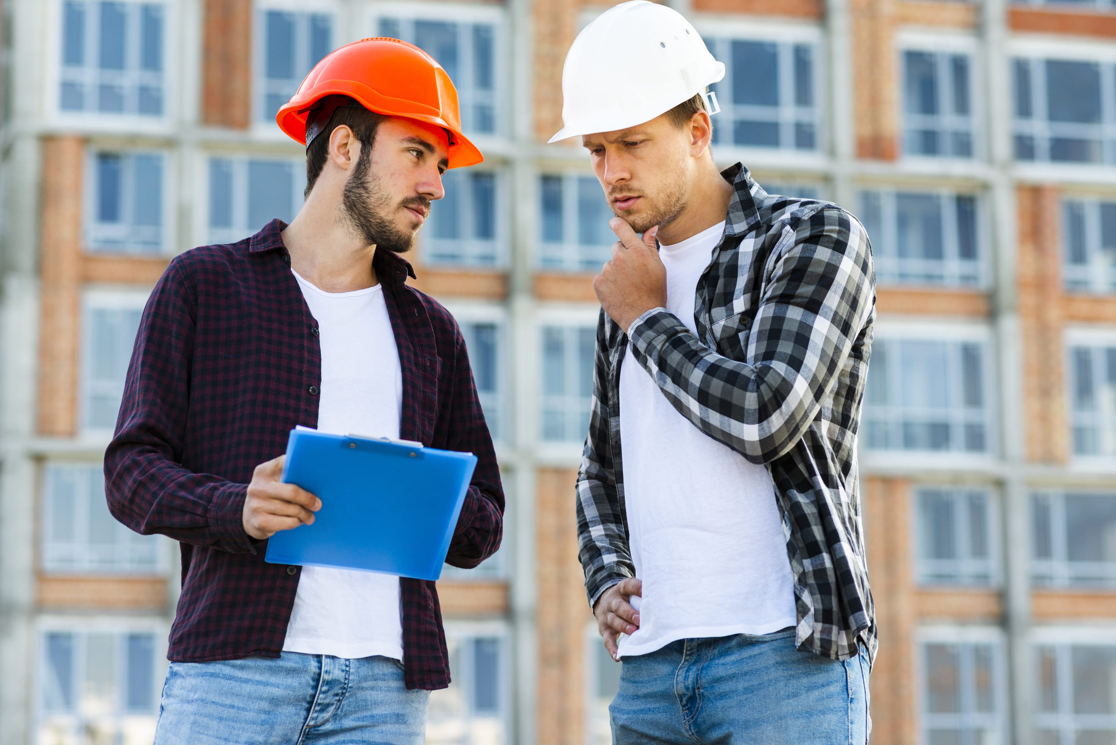 Two workers discuss plans outside a new building