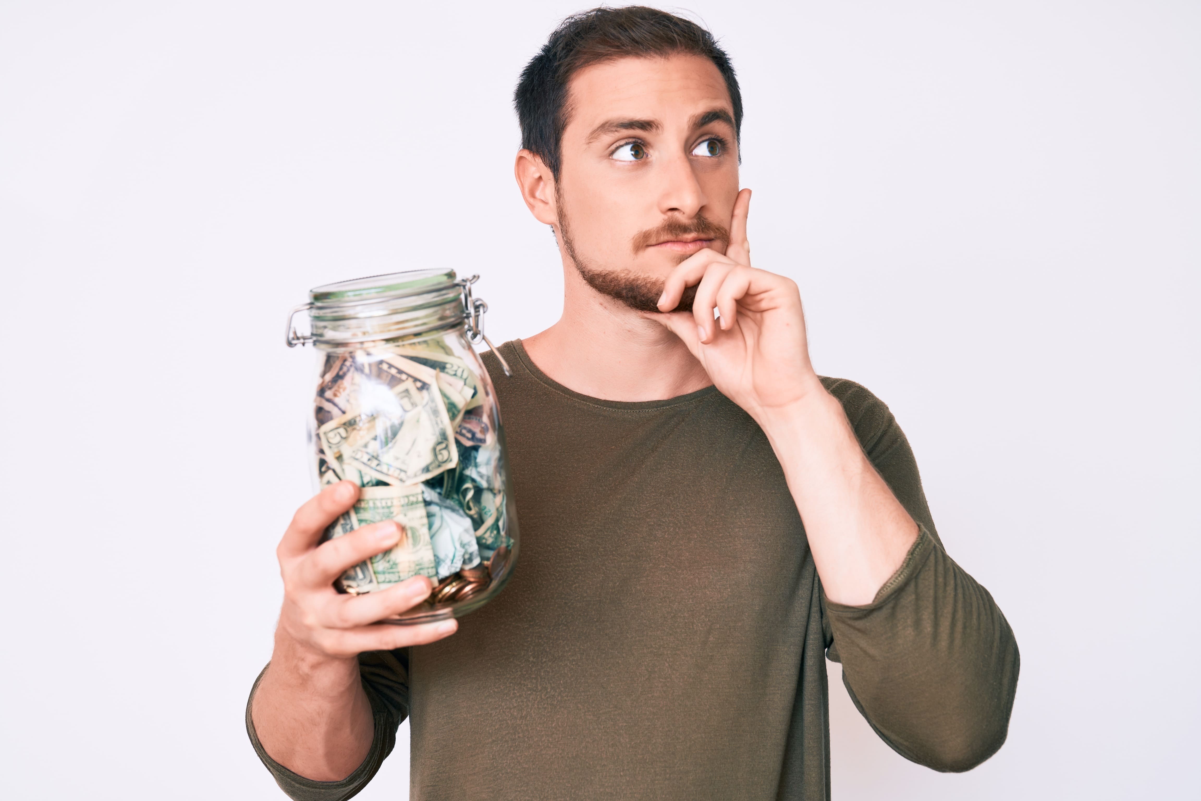A man holds a jar of money, thinking