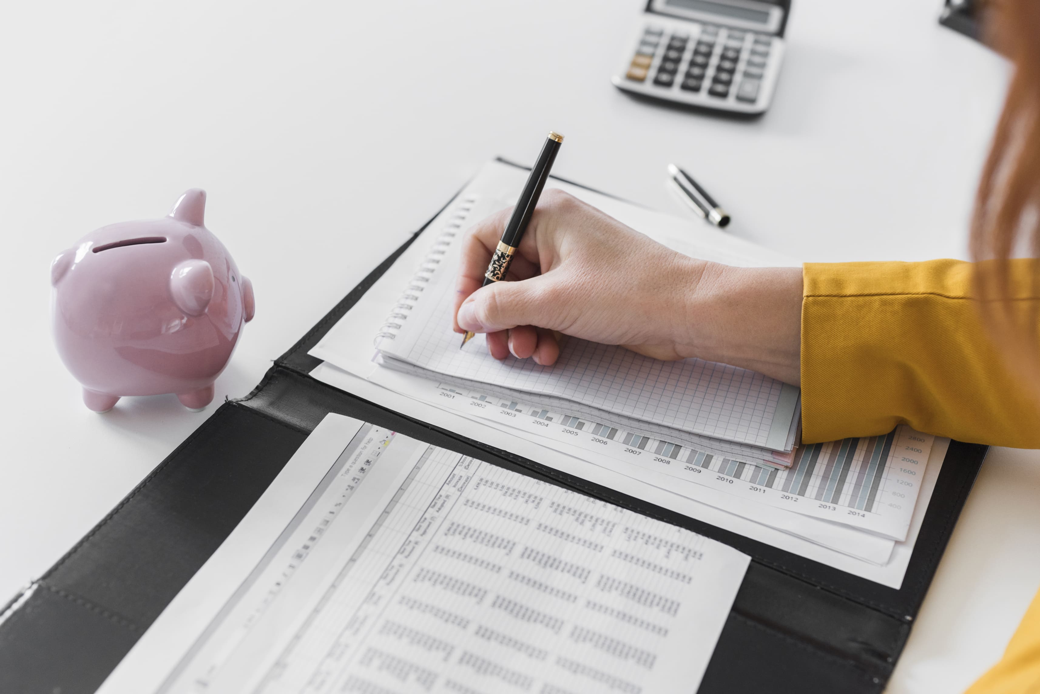 Woman writes notes near pink piggy bank and calculator