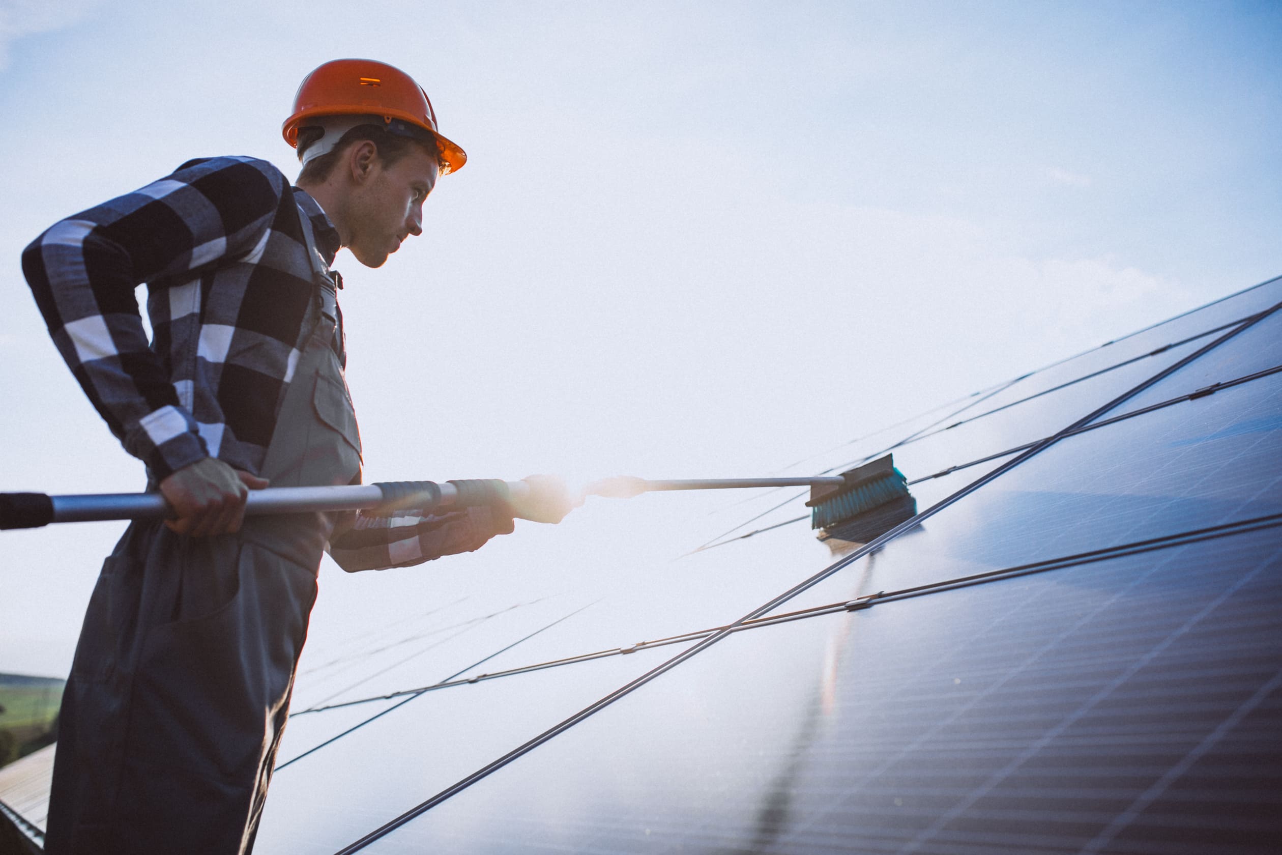Worker cleans solar panel with long brush tool