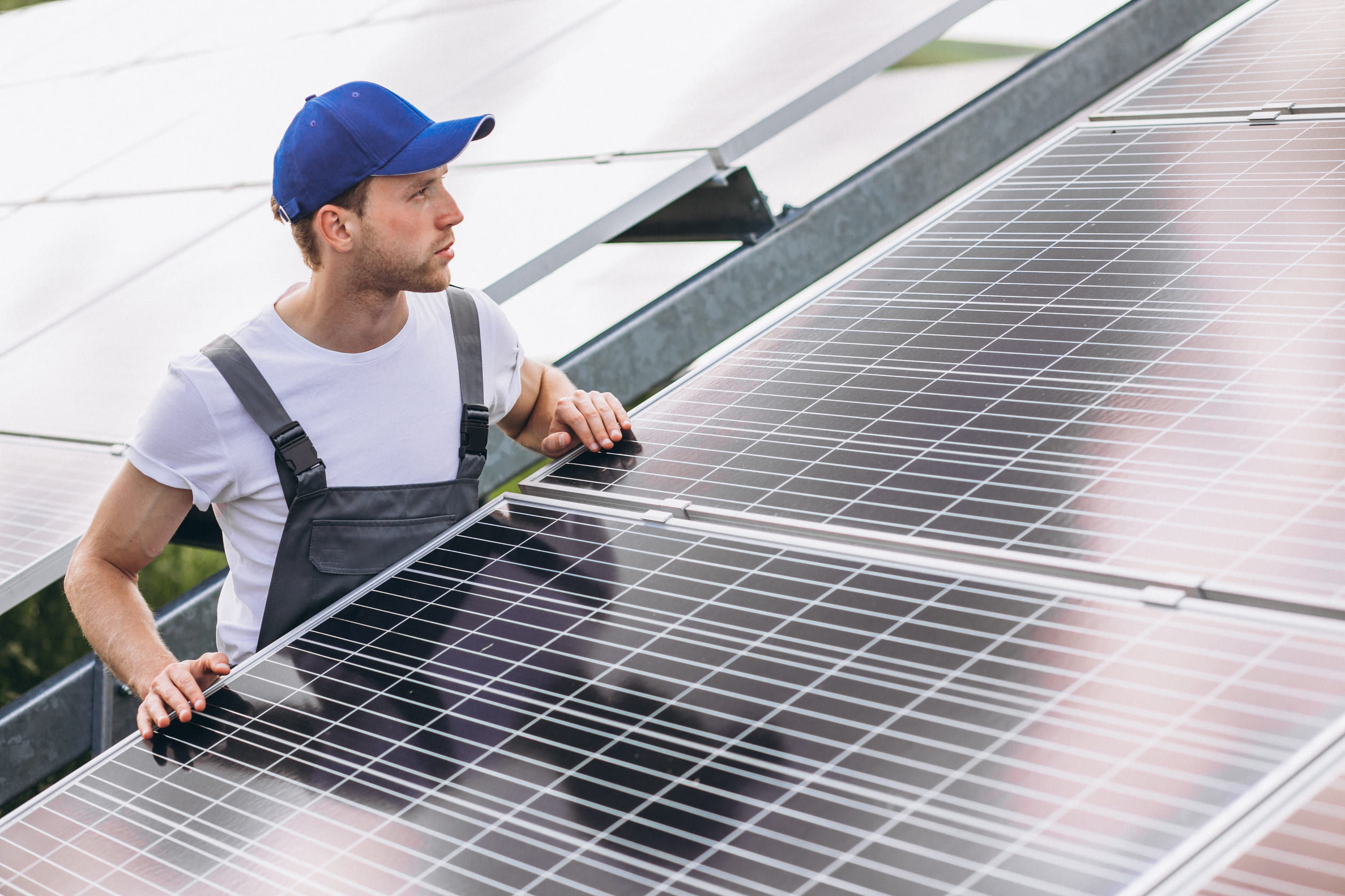 Worker inspects solar panel with blue hat and overalls