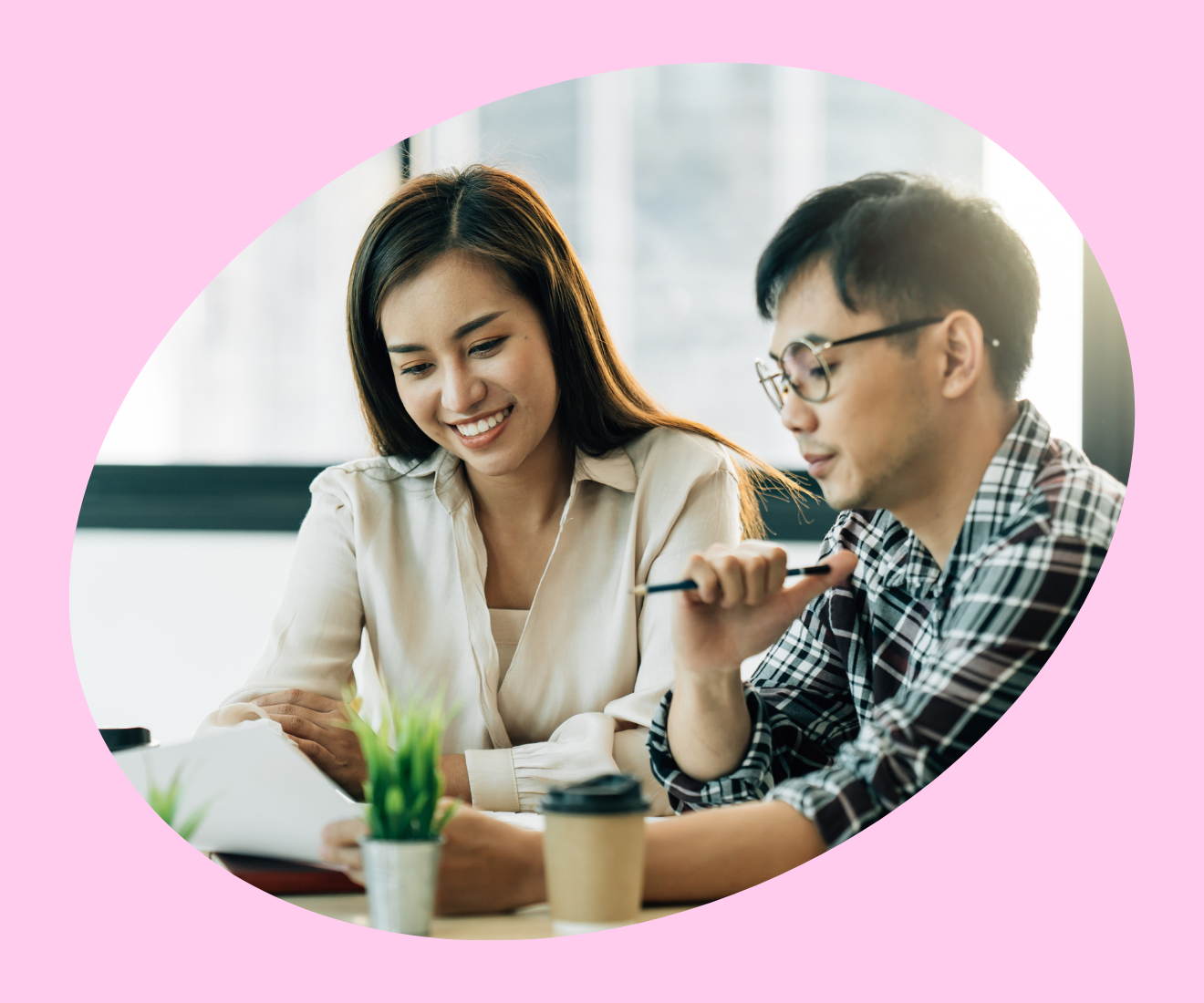 Två unga personer samarbetar vid ett bord med dokument och kaffemuggar.