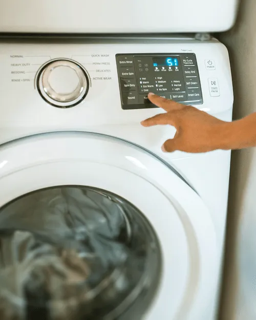 Hand drückt eine Taste am Bedienfeld einer weißen Waschmaschine mit digitaler Anzeige.
