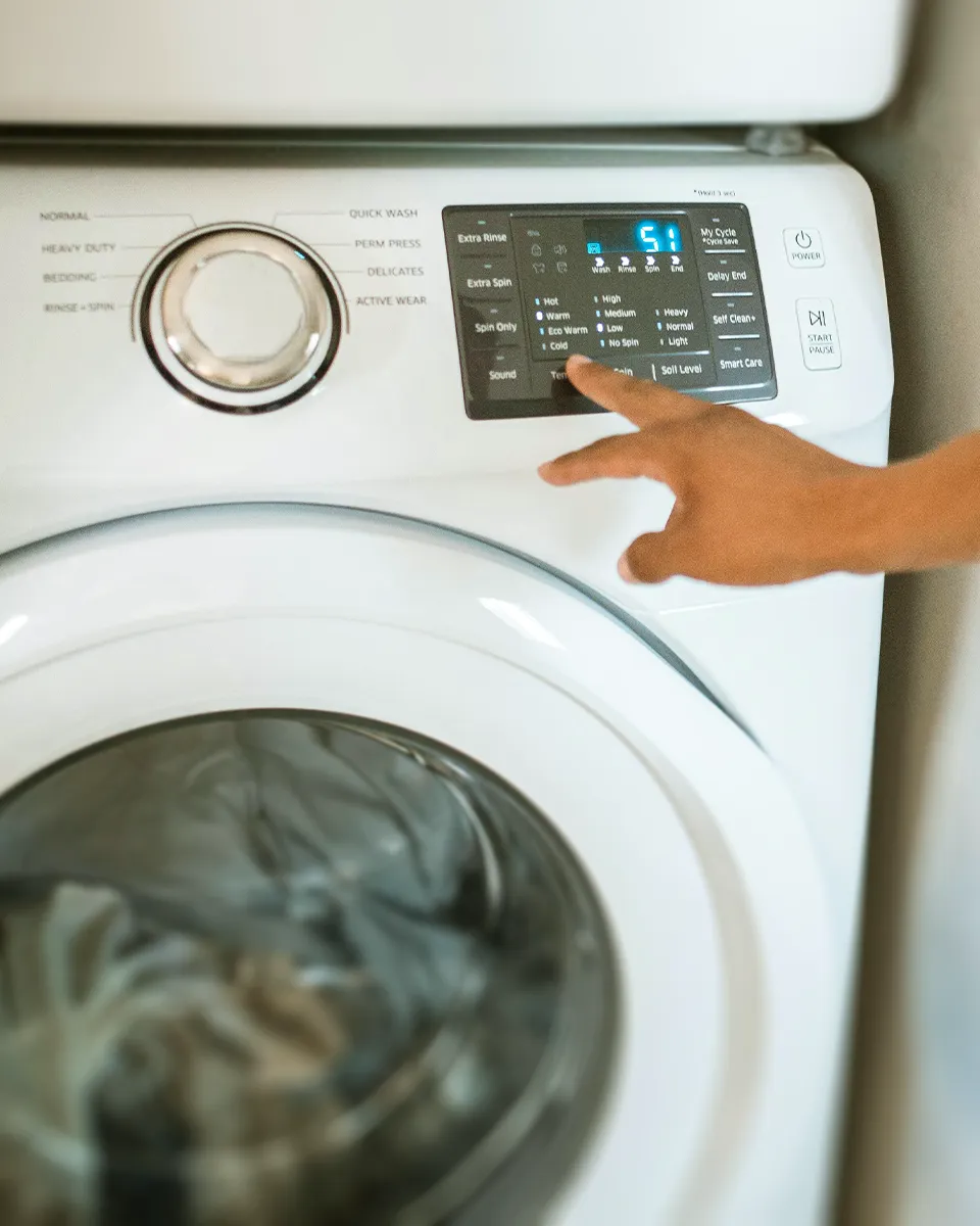 Hand drückt eine Taste am Bedienfeld einer weißen Waschmaschine mit digitaler Anzeige.