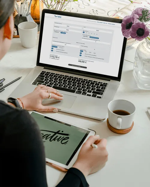 Person nutzt Laptop mit Lezzy-Website und Tablet mit kreativem Schriftzug, neben Kaffeetasse und Blumen auf dem Tisch.