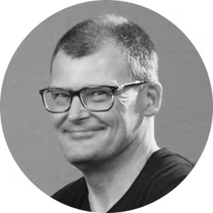 Schwarz-weiß-Porträt eines Mannes mit Brille und kurzem Haar, der leicht lächelt.