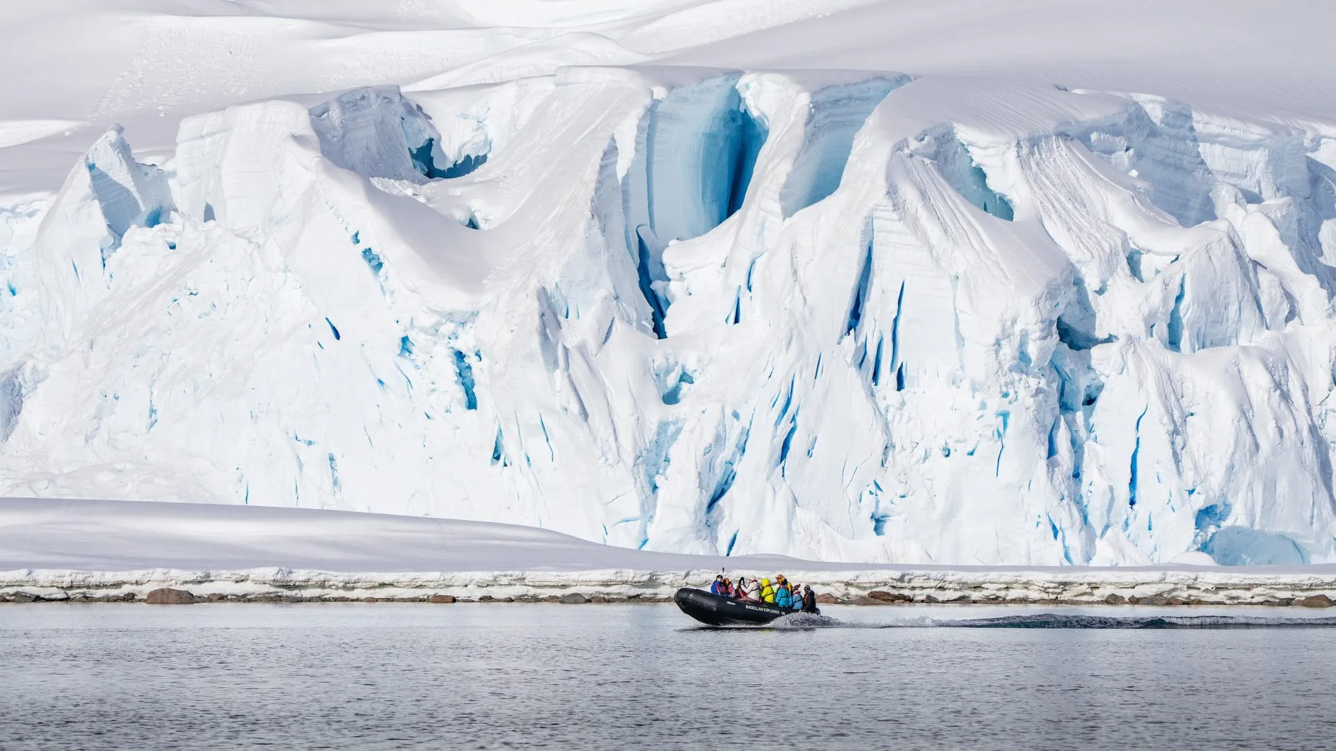 Group of people in a black inflatable boat near towering icy glacier cliffs.