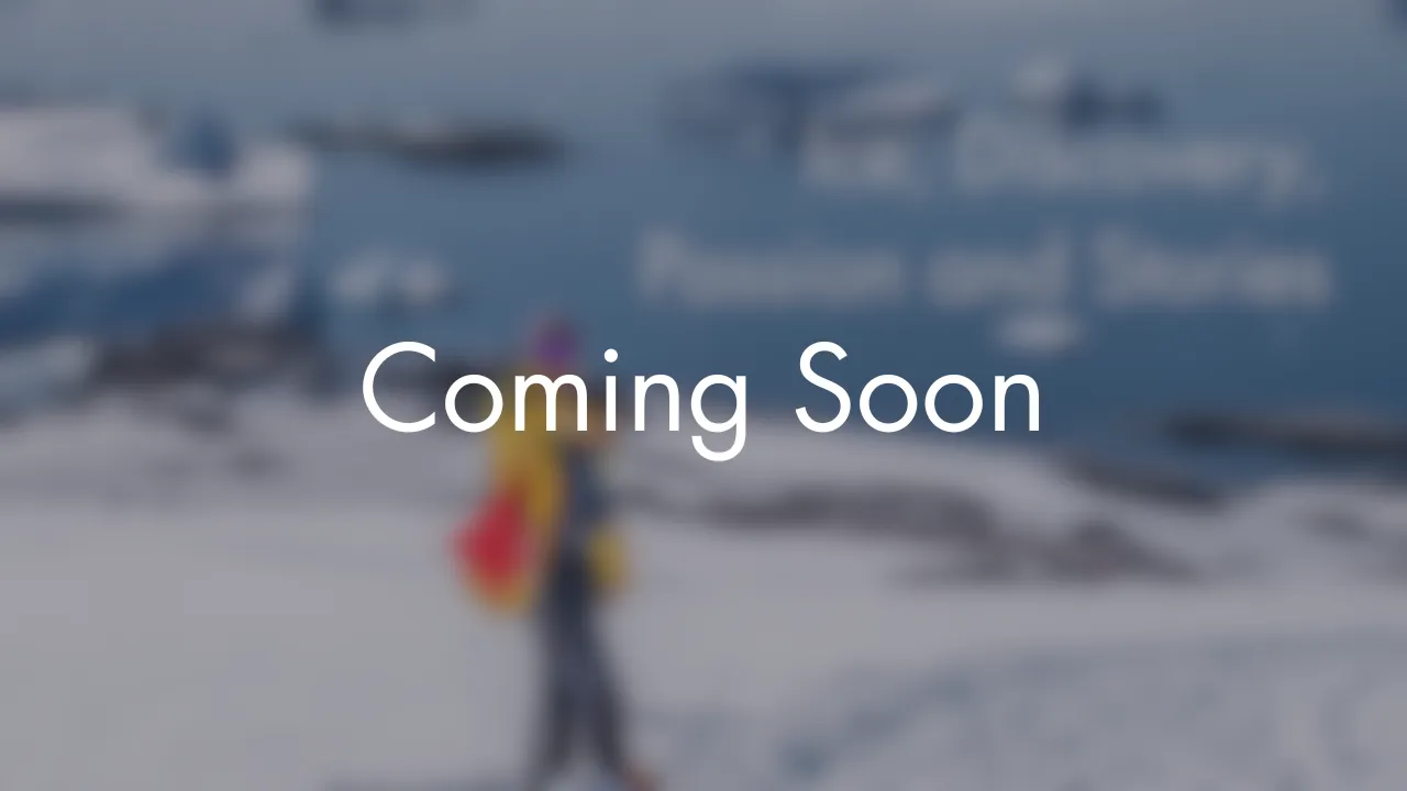 Person wearing a yellow jacket and carrying a red backpack walking on a snowy landscape near a body of water.