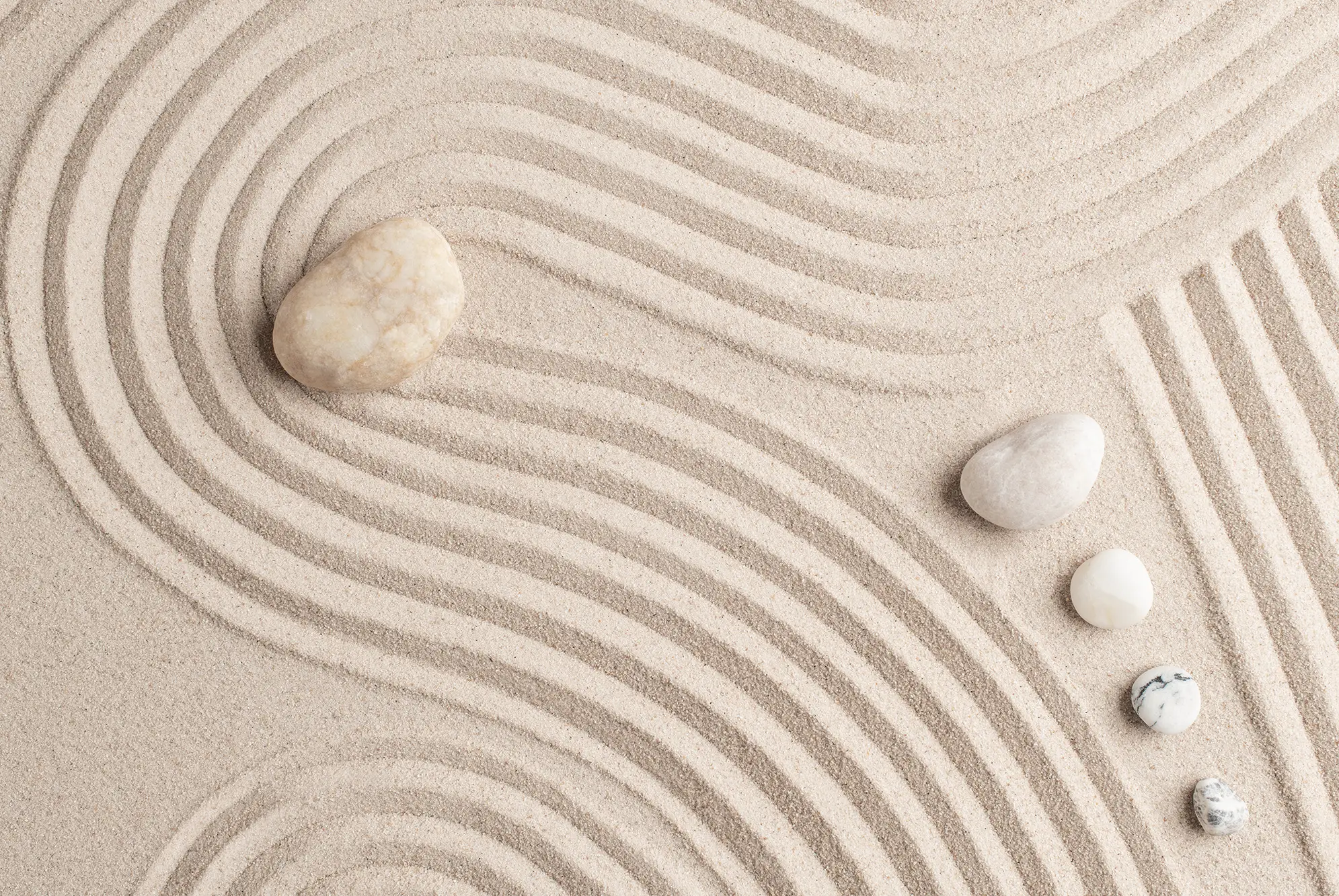 Heller Zen-Sand mit weich geschwungenen Linien und mehreren runden Steinen in unterschiedlichen Größen.
