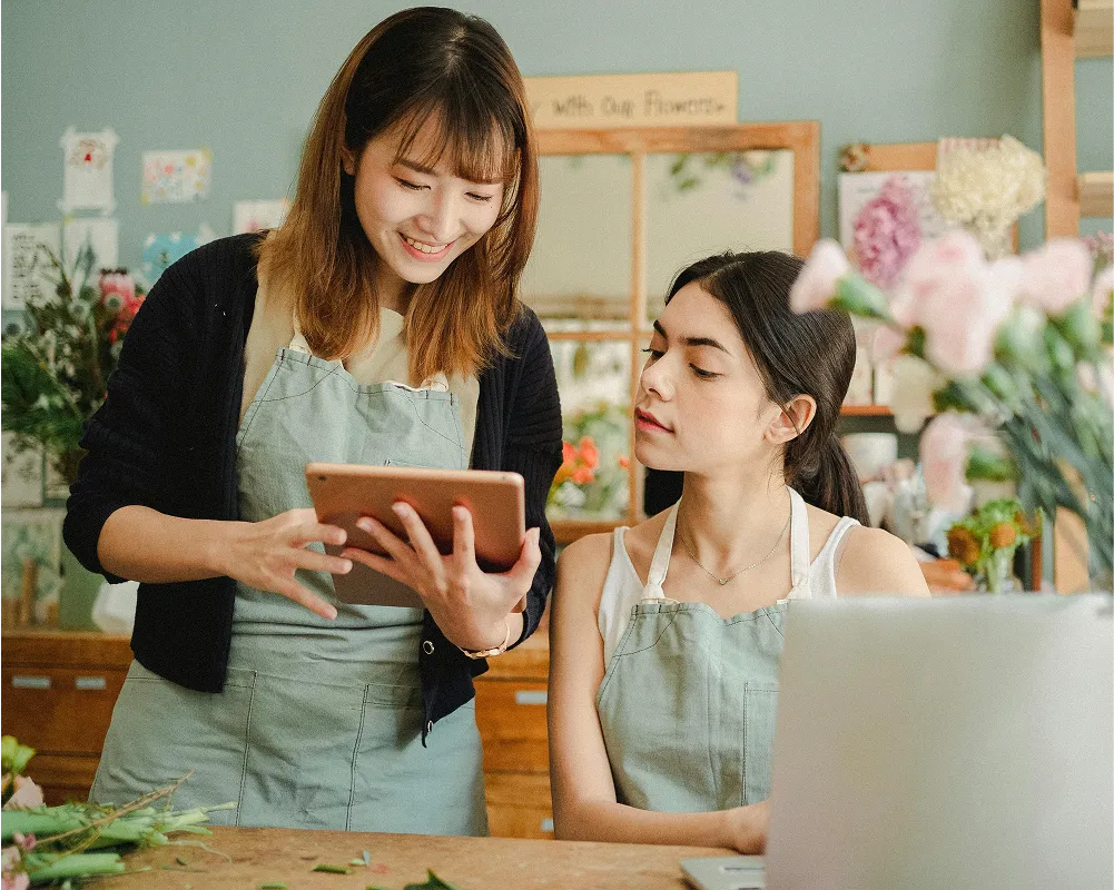 Two woman working, one is holding a tablet showing the other while smiling