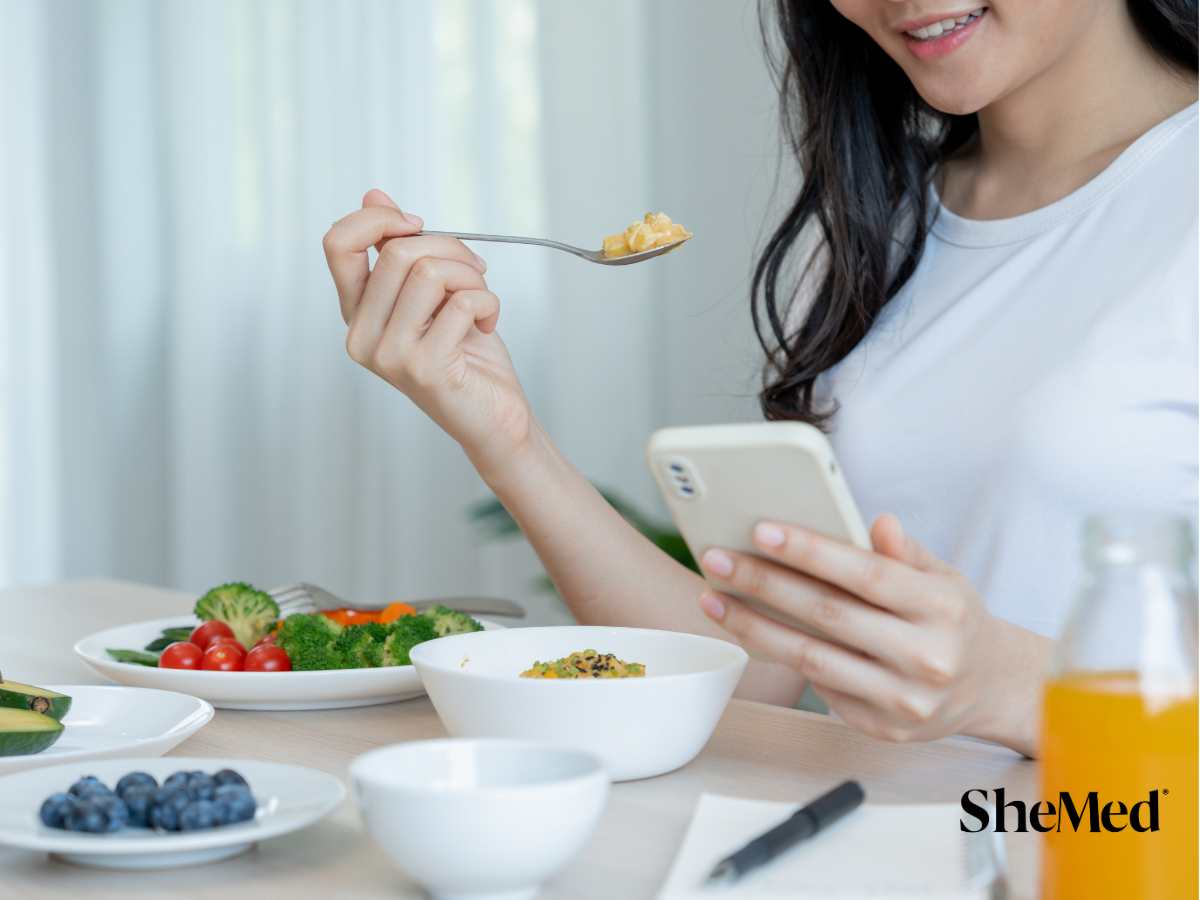 A girl smiling as she enjoys a colourful bowl of healthy salad, filled with fresh vegetables and greens, with SheMed logo at the corner.