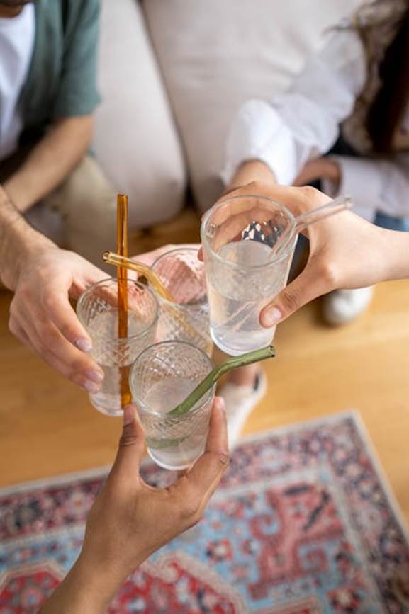 Above view of friends toasting with glasses of water and colored straws indoors.