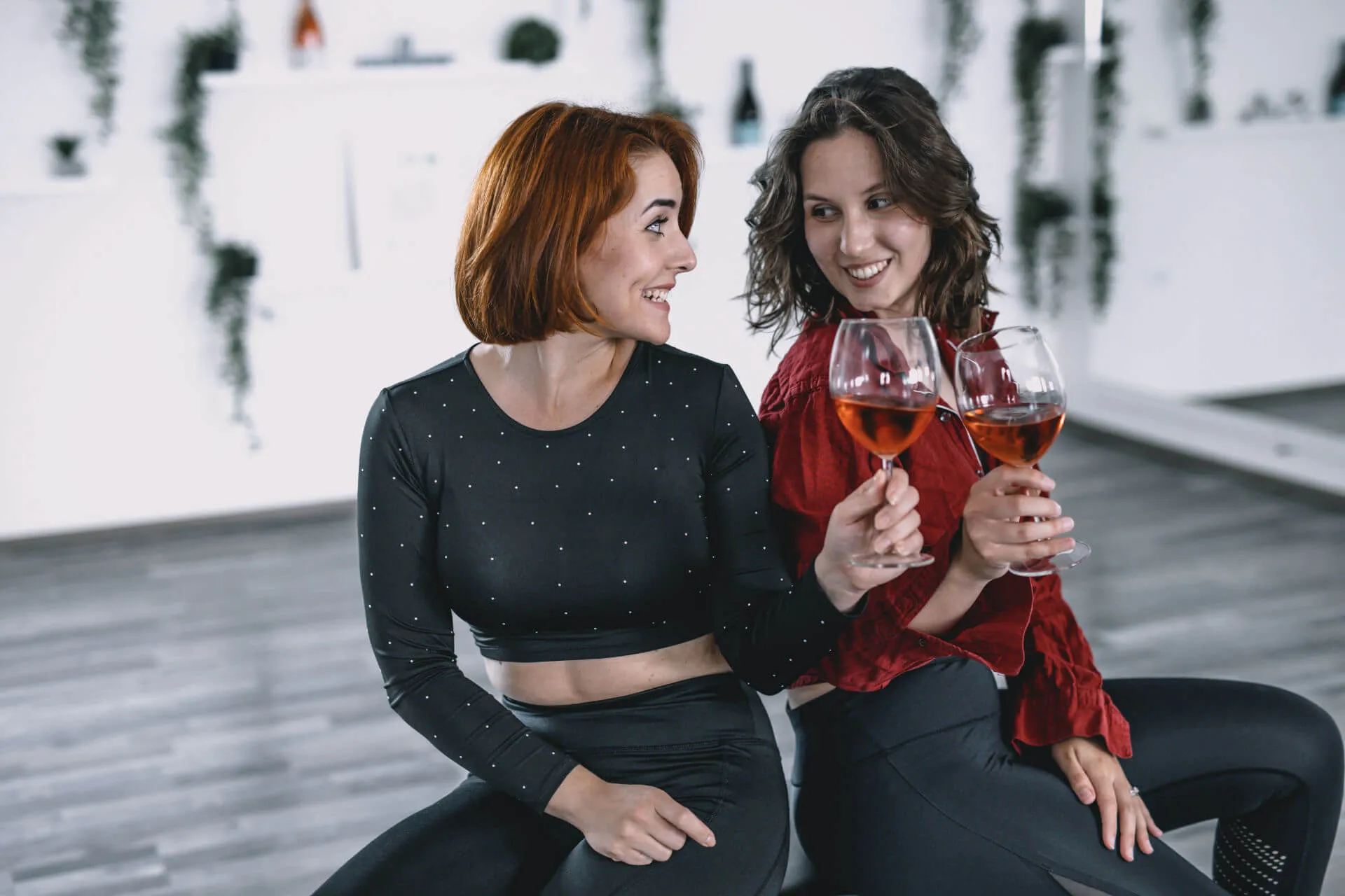 Dvije žene sjede na stolicama i nazdravljaju s vinom