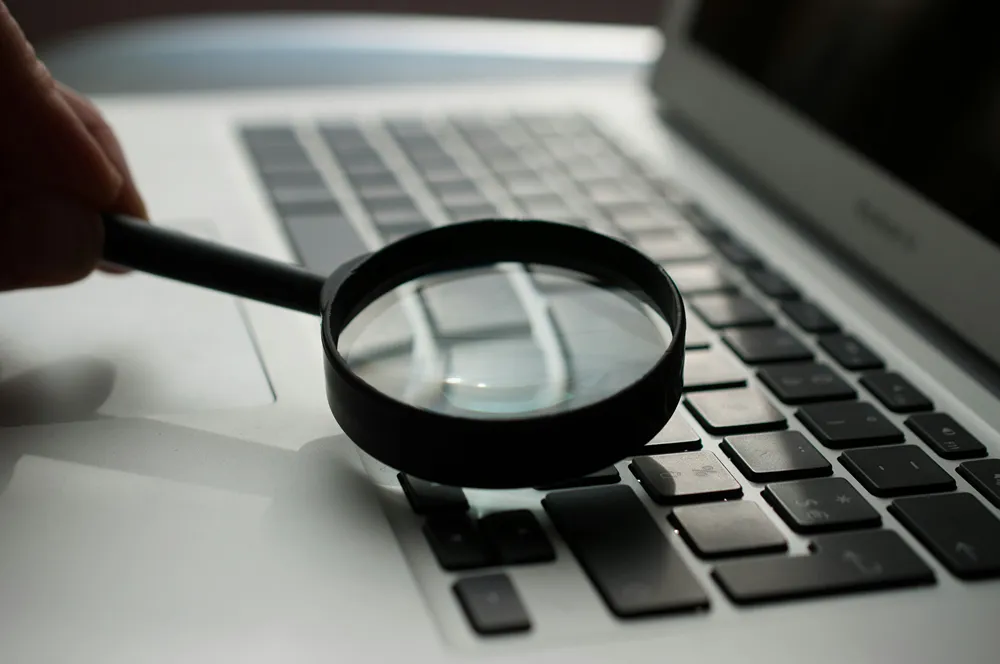 Magnifying glass over a laptop keyboard, illustrating penetration test scope versus depth
