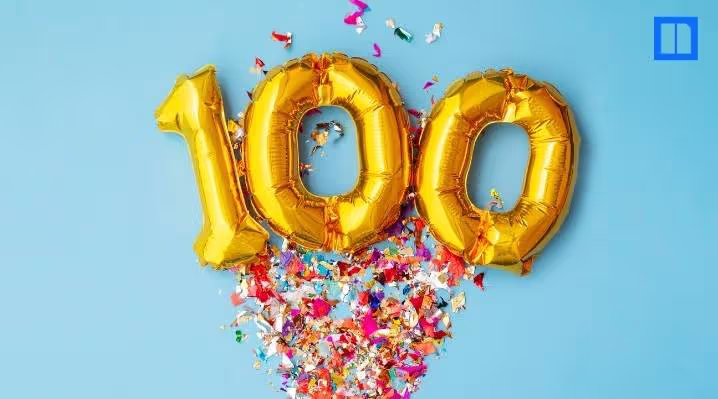 Gold "100" number balloons centered on a bright blue background with colorful festive confetti, representing a 100th day of school celebration.